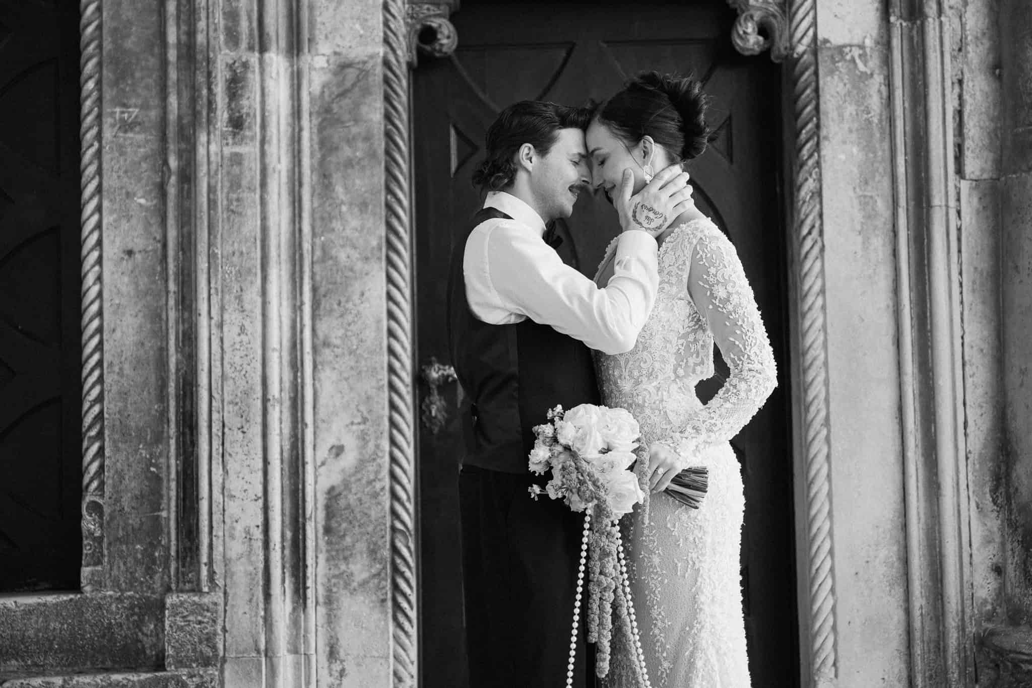 Nježan crno-bijeli portret; mladenci zatvorenih očiju naslonjeni čelima jedno na drugo okruženi povijesnim kamenim stupovima u Dubrovniku.