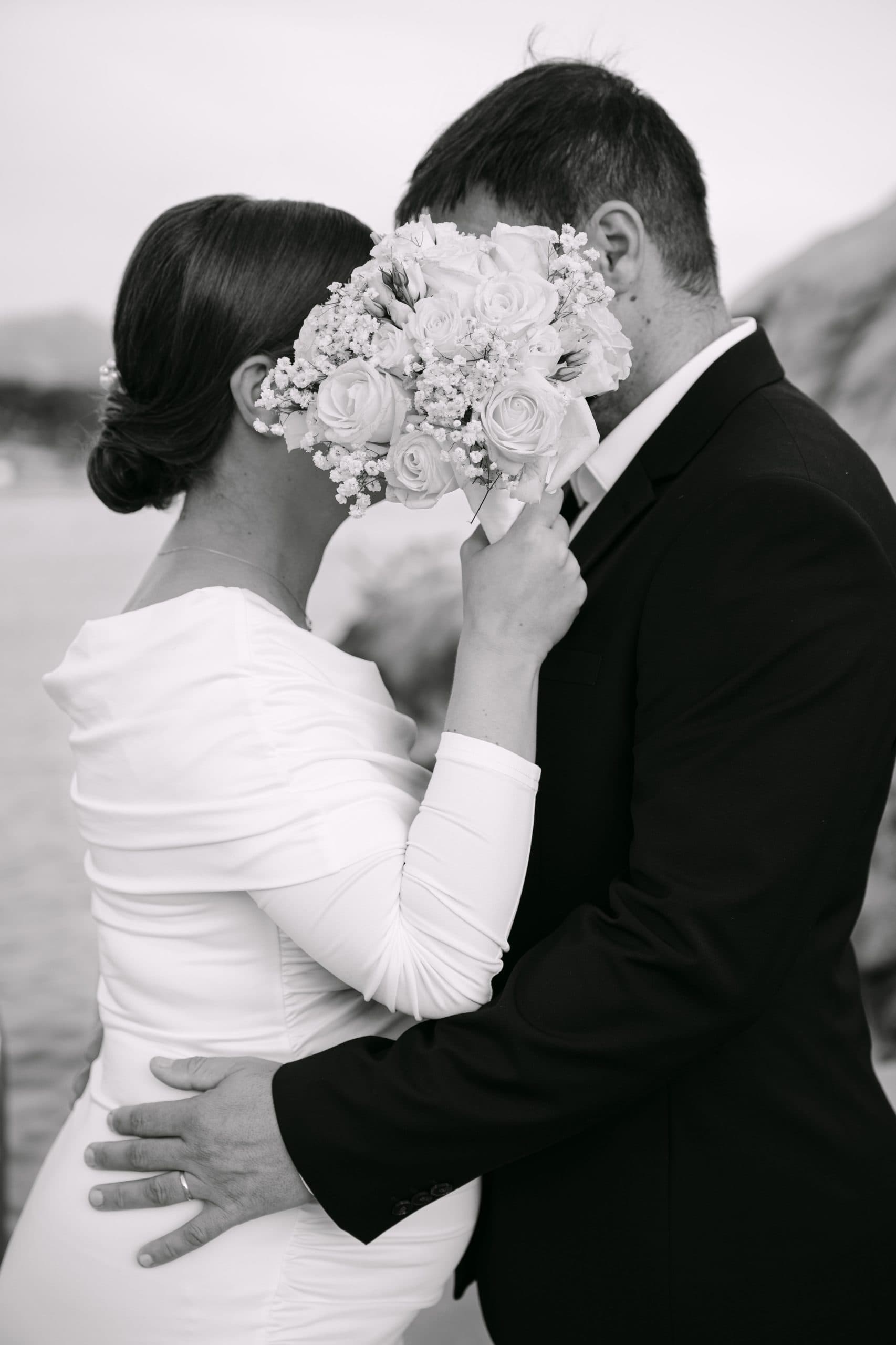 Vjenčani par s cvjetnim buketom zaklonjen licem.