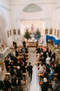 Široki kadar crkvenog vjenčanja u Omišu gdje mladenci hodaju središnjim prolazom prema oltaru okruženi uzvanicima u klupama.