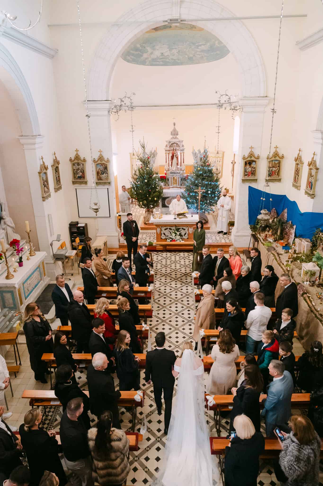 Široki kadar crkvenog vjenčanja u Omišu gdje mladenci hodaju središnjim prolazom prema oltaru okruženi uzvanicima u klupama.