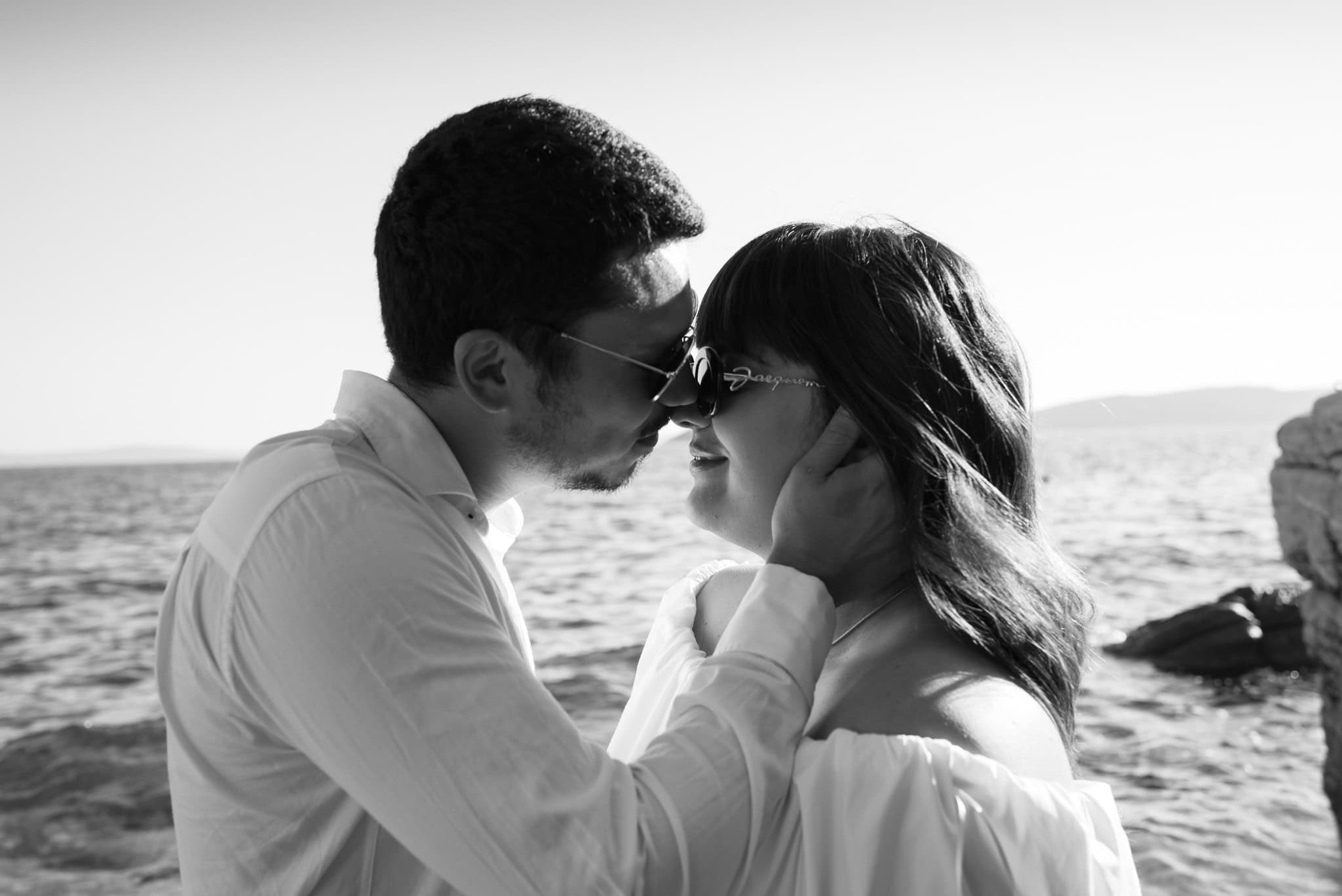 Dodir nosevima i zatvorene oči; intimna crno-bijela fotografija zaručenog para s rukom na obrazu.