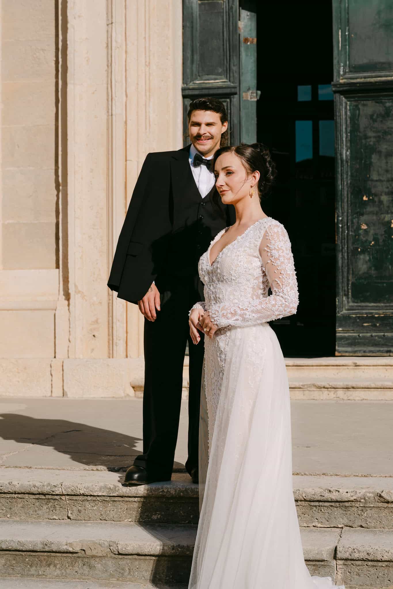 Nježni portret mladenaca na otvorenom; par pozira u punoj visini ispred masivnih starinskih drvenih vrata s izraženom teksturom i povijesnim šarmom grada Dubrovnika.