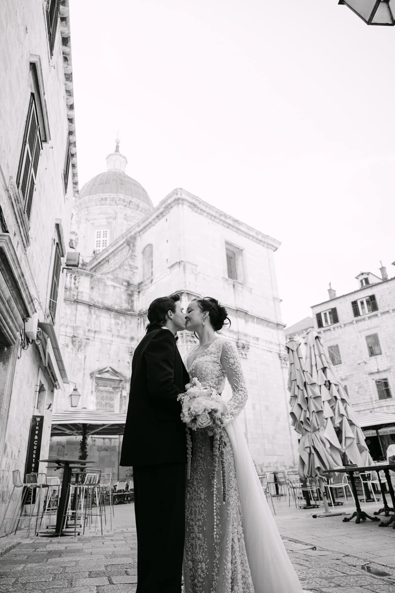 Dubrovnik wedding session na otvorenom – romantičan crno-bijeli kadar; mladenci se nježno ljube na povijesnom trgu ispred impresivne arhitekture Starog grada i kupole katedrale.