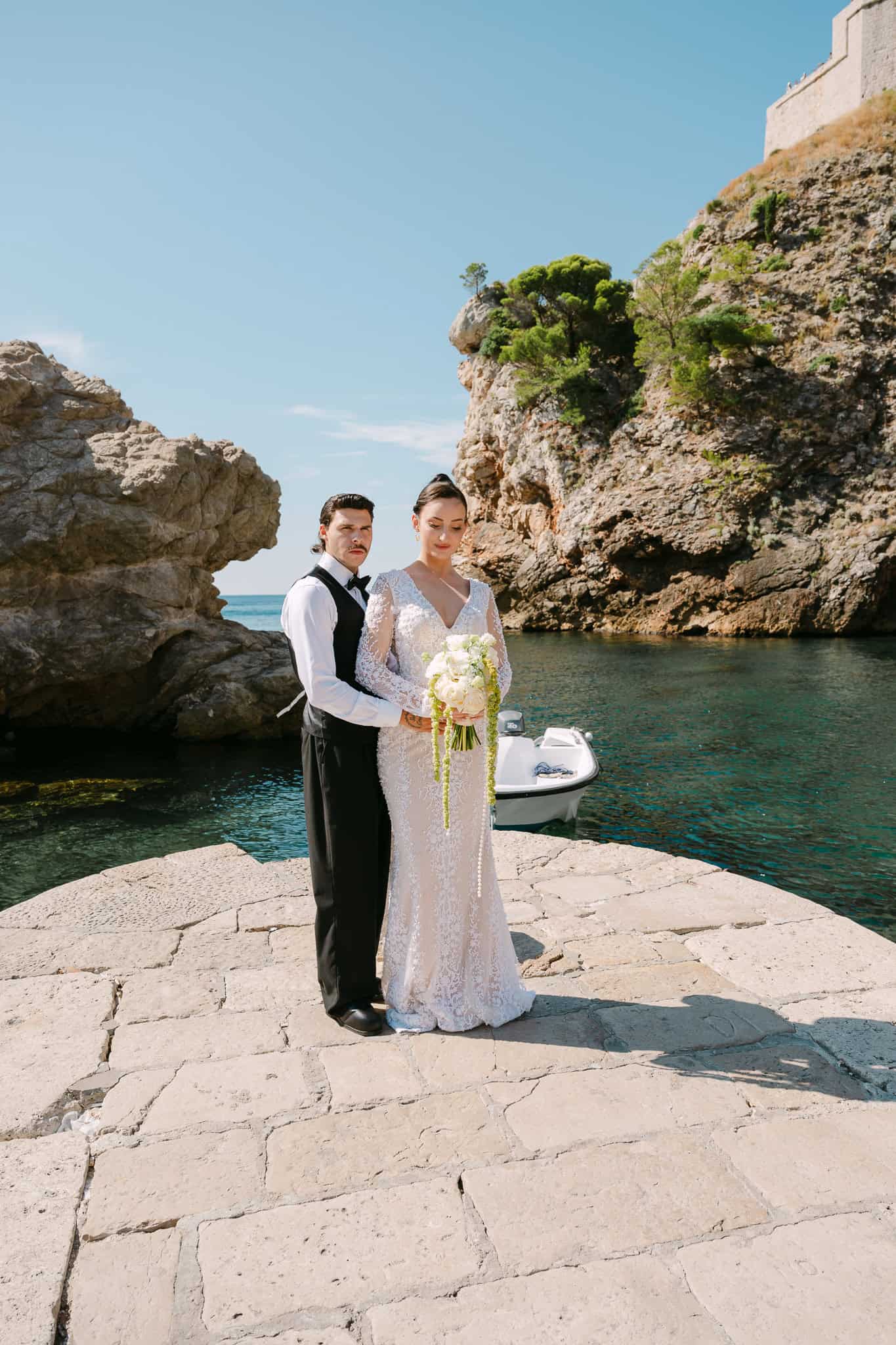 Vjenčanje Dubrovnik, Lovrijenac - ljetni kadar; elegantni mladenci poziraju na starom kamenom mulu s pogledom na mirno more i visoke litice.