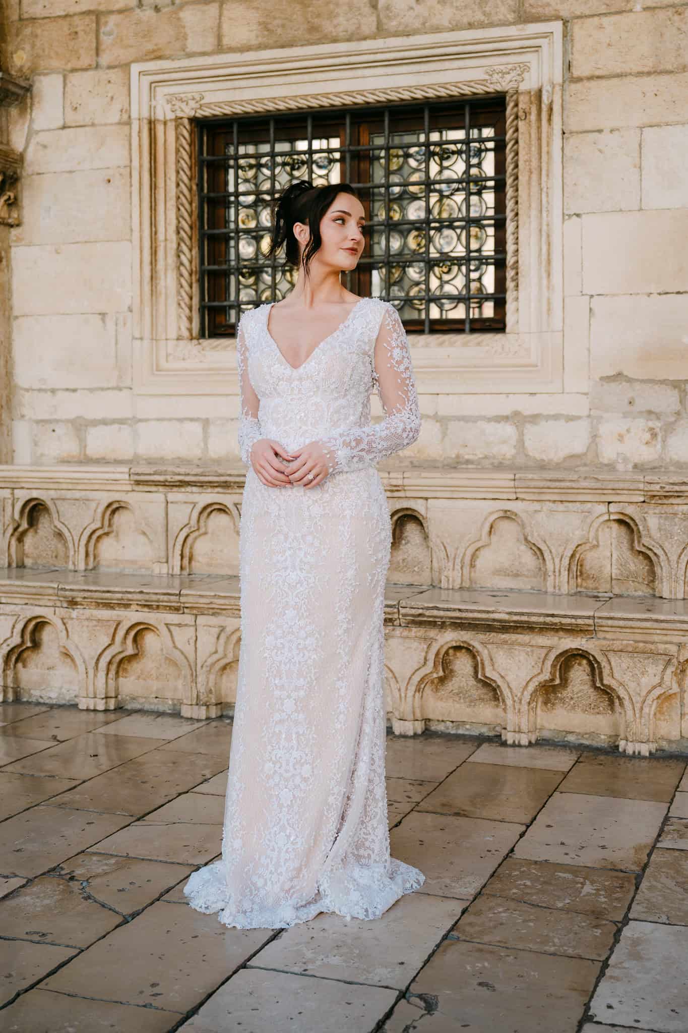 Dubrovnik vjenčanje – elegantni portret mladenke; nevjesta u čipkastoj vjenčanici pozira ispred povijesnog kamenog zida s ukrasnim prozorom u Starom gradu.