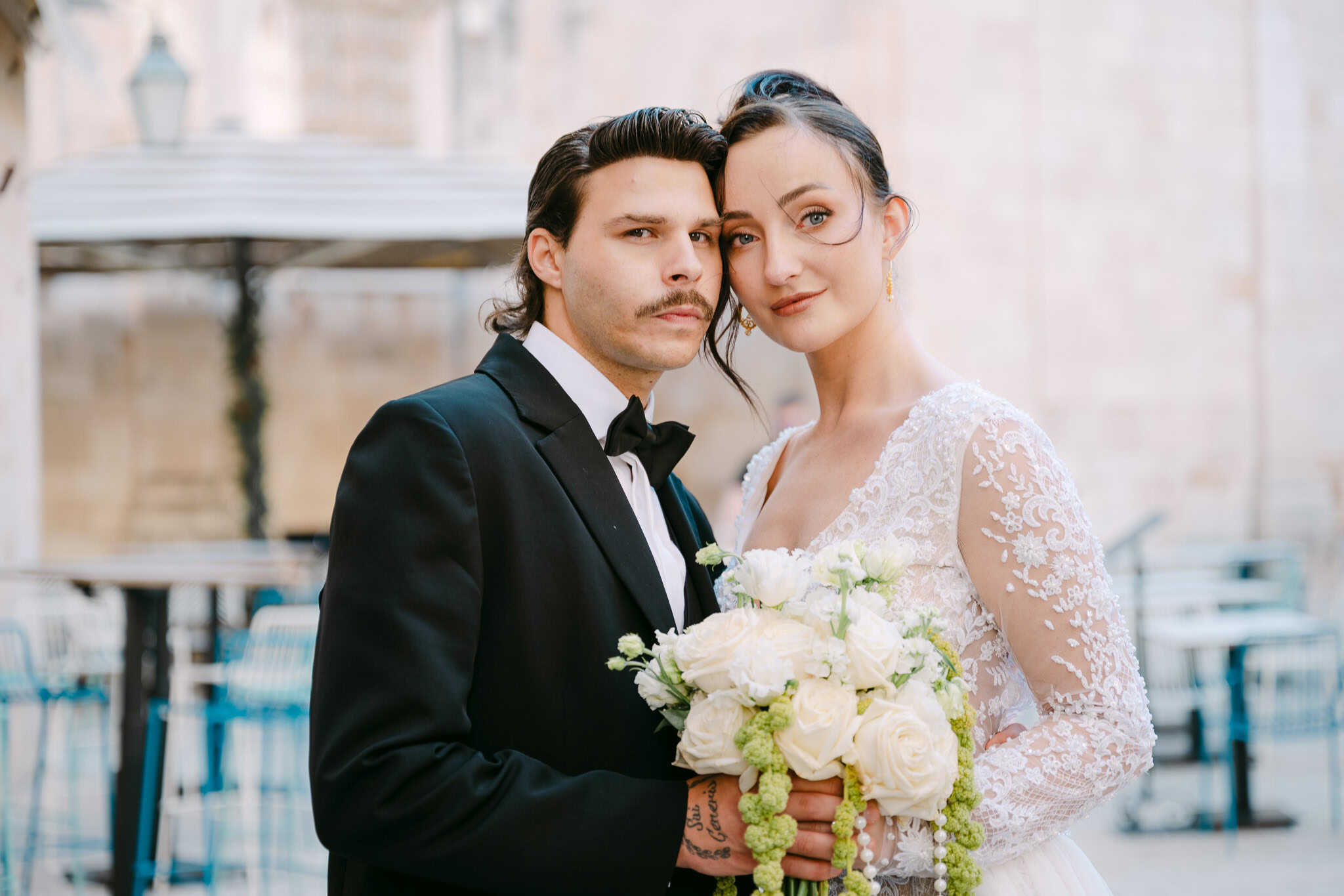 Vjenčanje u Dubrovniku na otvorenom – bliski portret mladenaca; elegantni par s bogatim bijelim bidermajerom pozira na starogradskom trgu.