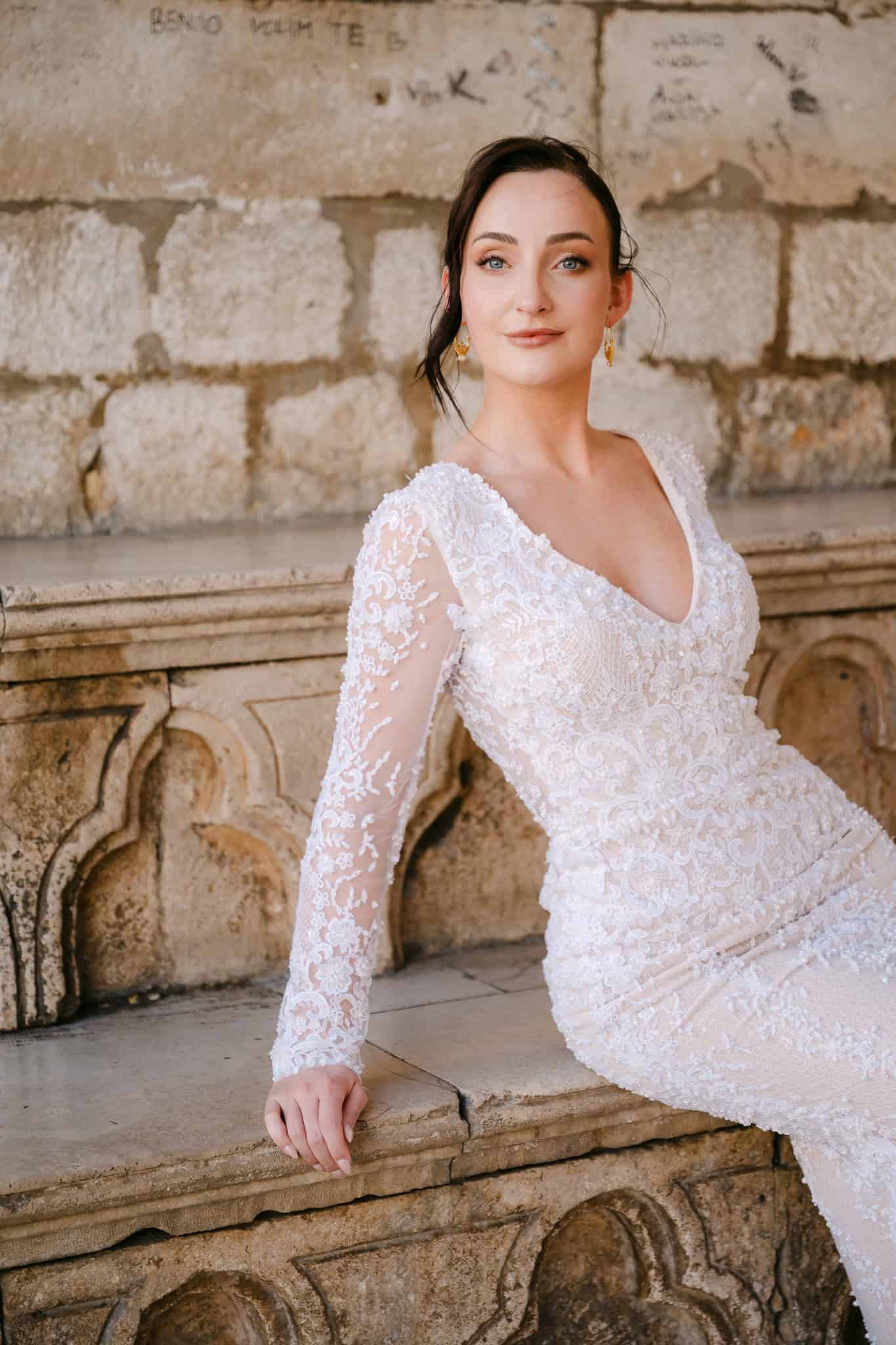 Dubrovnik wedding session - elegantan portret mladenke; nevjesta u bijeloj čipkastoj vjenčanici pozira naslonjena na staru kamenu klupu s povijesnim uklesanim detaljima.