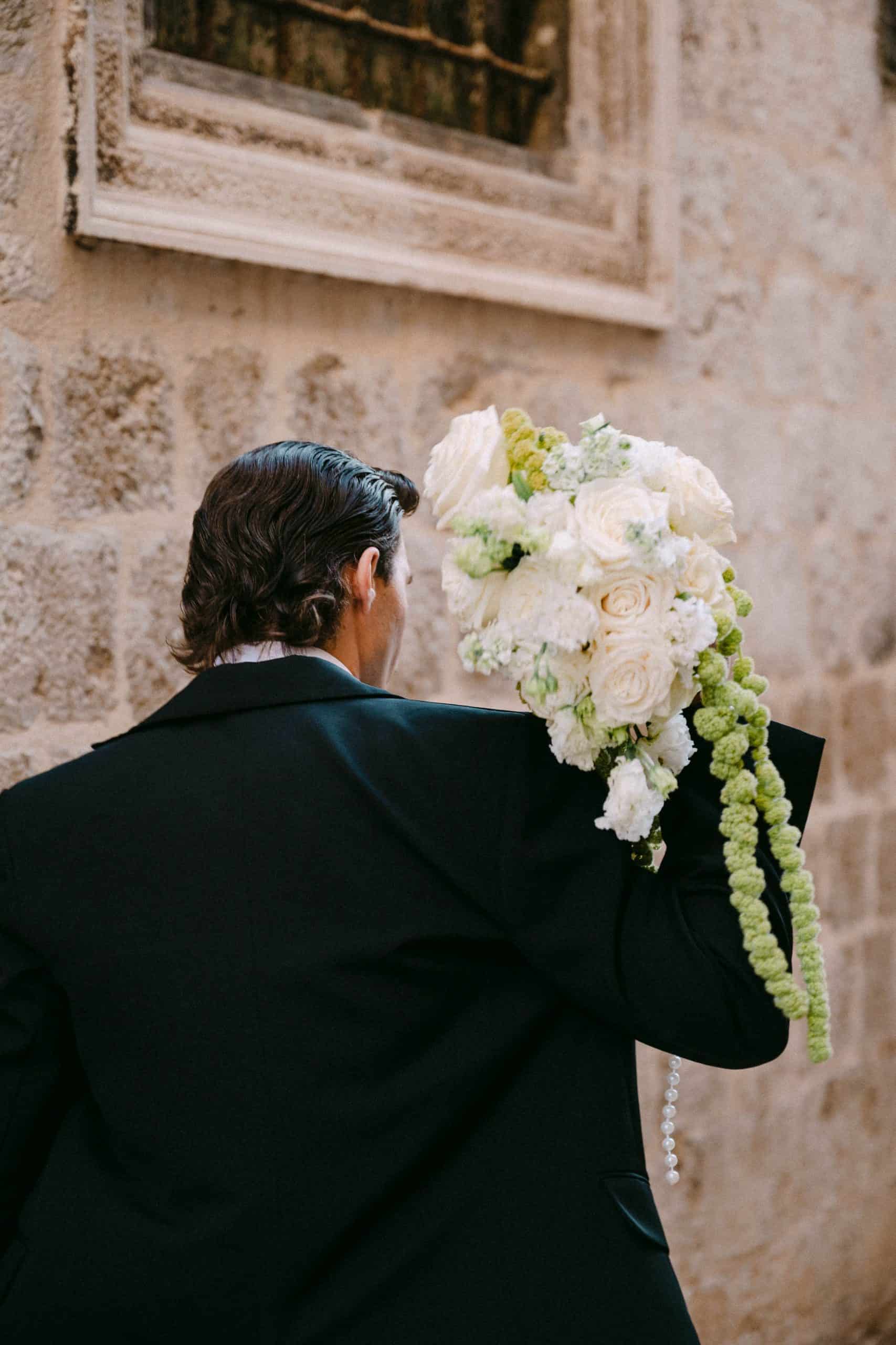 Mladoženja s buketom bijelih cvjetova na ulici.