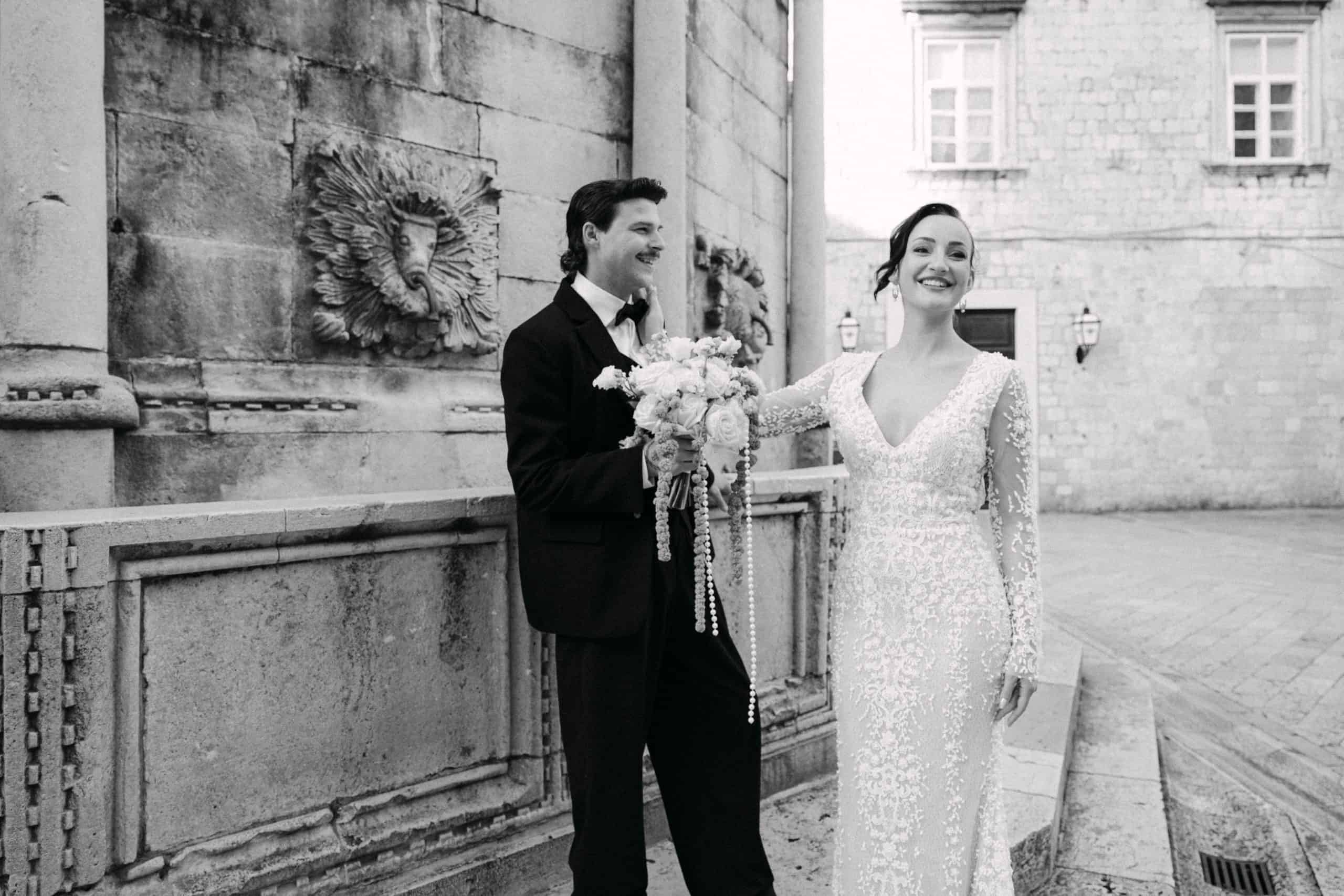 Dubrovnik, Stradun - nasmiješeni mladenci na kamenim skalinama; crno-bijeli vjenčani portret ispred povijesne fontane gdje mladoženja drži buket.