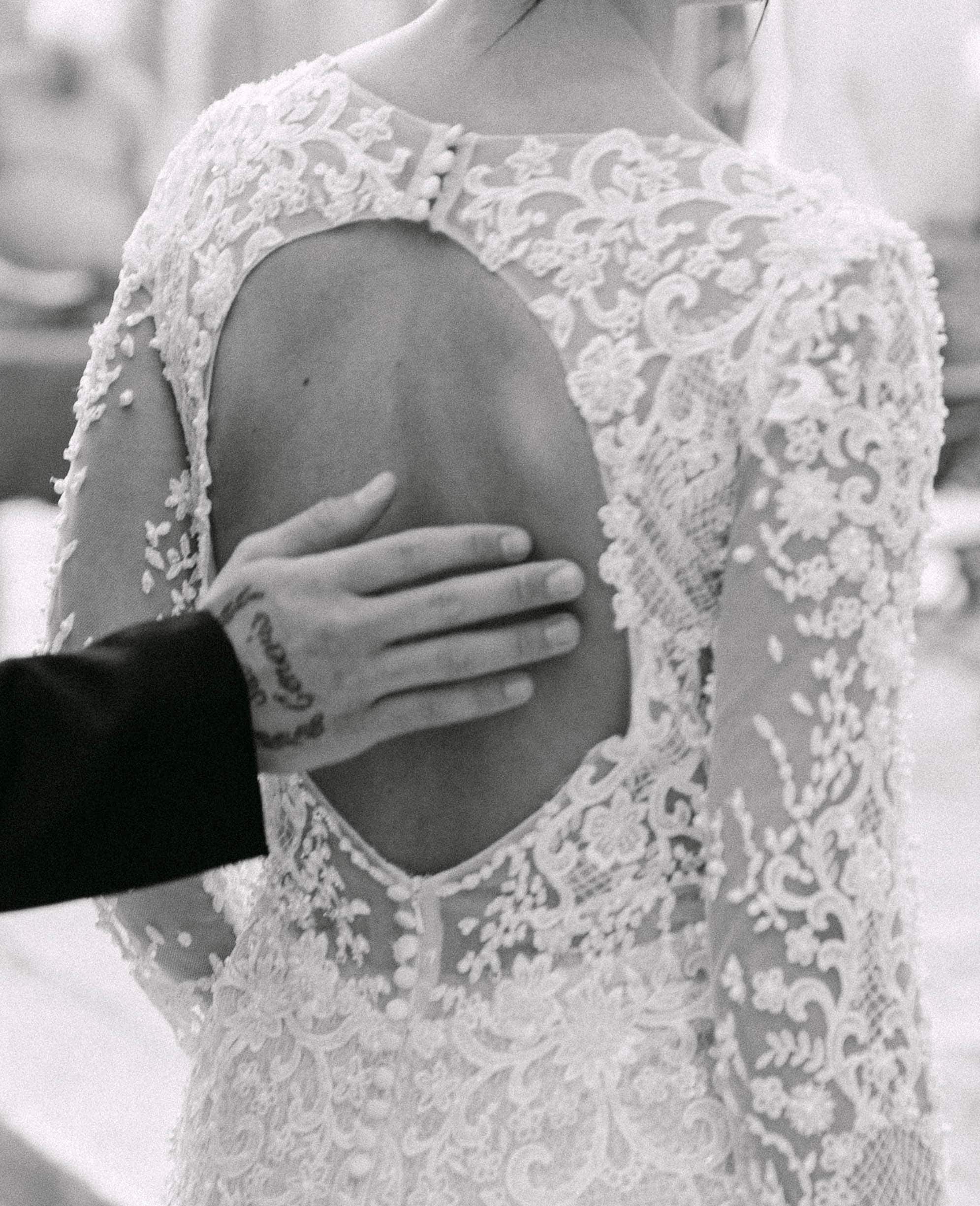 Dubrovnik wedding session - krupni kadar vjenčanice i nježnog dodira mladenaca; fokus na čipku i otvorena leđa.