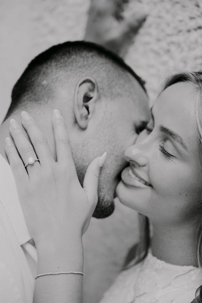 Crno-bijeli krupni plan lica zaručnika koji su naslonjeni jedno na drugo zatvorenih očiju, uz vidljiv zaručnički prsten na ruci.