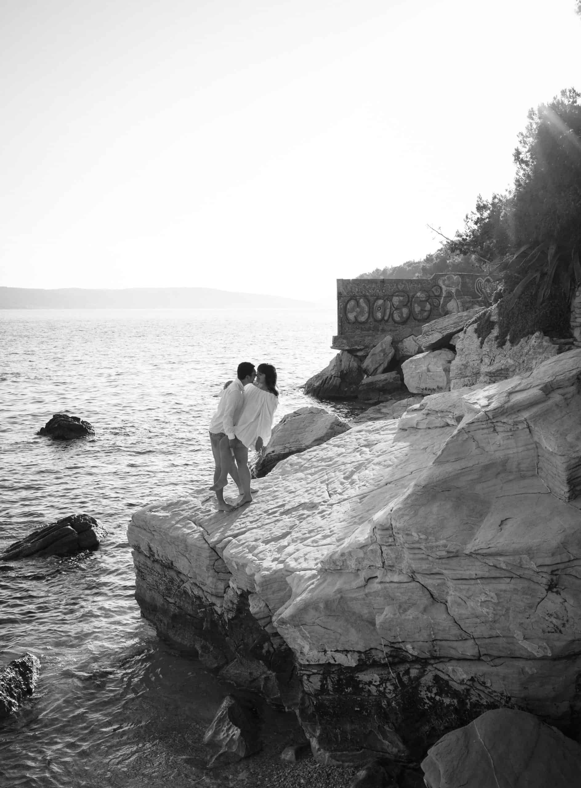 Crno-bijela fotografija zaručničkog para, Petra i Ivan, zagrljeni na stijeni uz more.