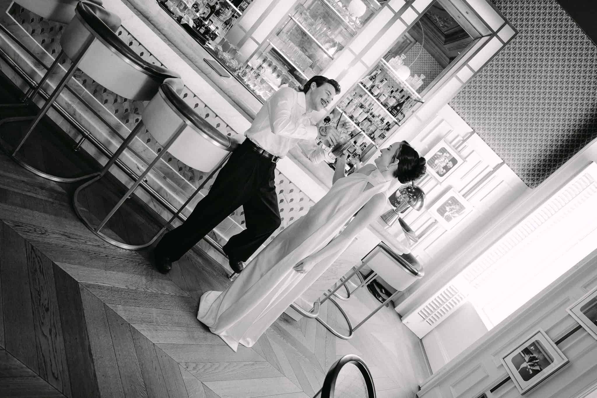 Vjenčanje u Dubrovniku – zabavan crno-bijeli kadar s nakošenom kompozicijom; par uživa u piću ispred stiliziranog hotelskog šanka.