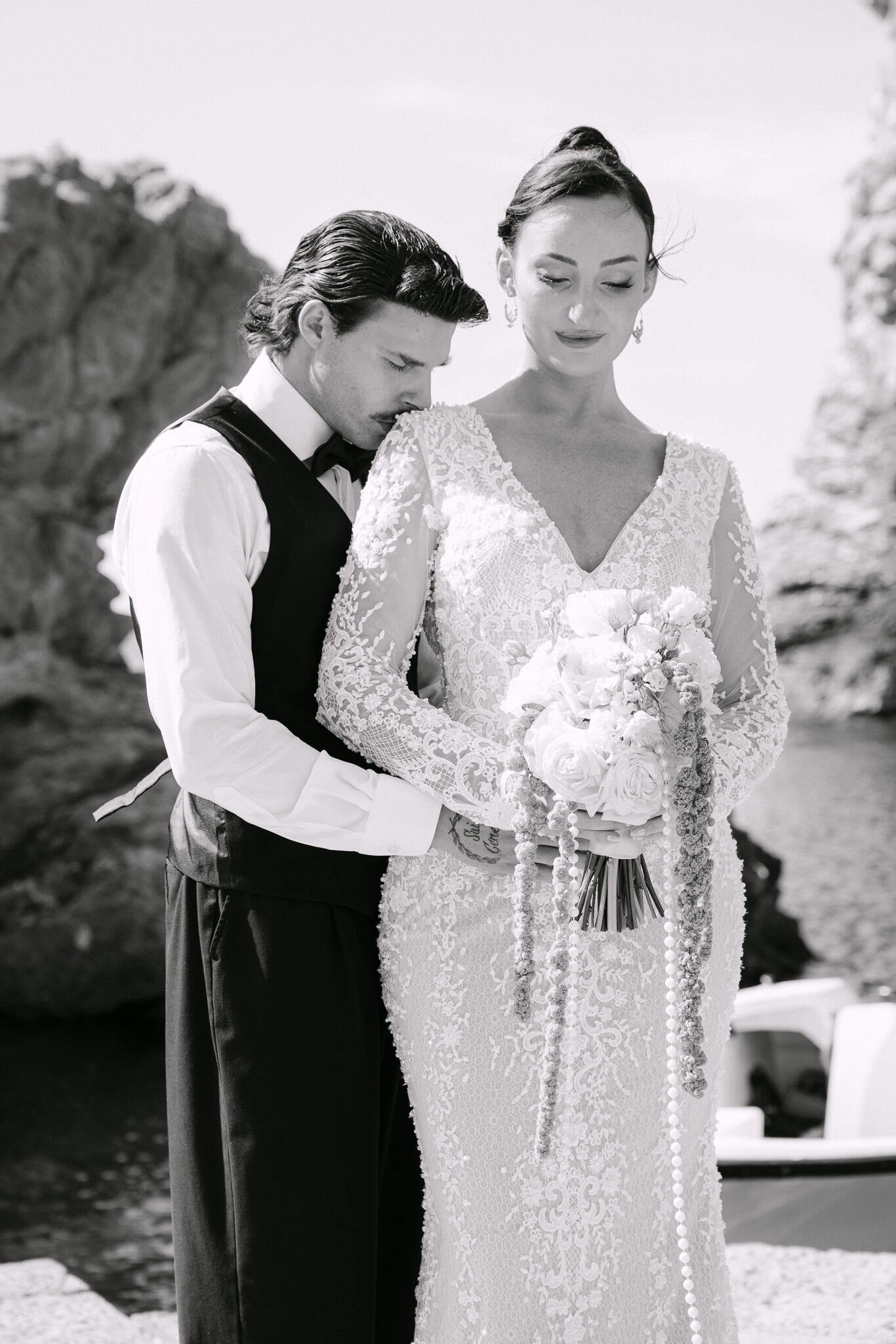 Dubrovnik wedding session - intimni crno-bijeli portret; mladoženja nježno ljubi mladenku u rame ispred morskog pejzaža i stijena.