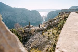 Široki pejzažni kadar mladenaca koji stoje na kamenom vidikovcu iznad kanjona rijeke Cetine tijekom svadbenog sessiona u Omišu.