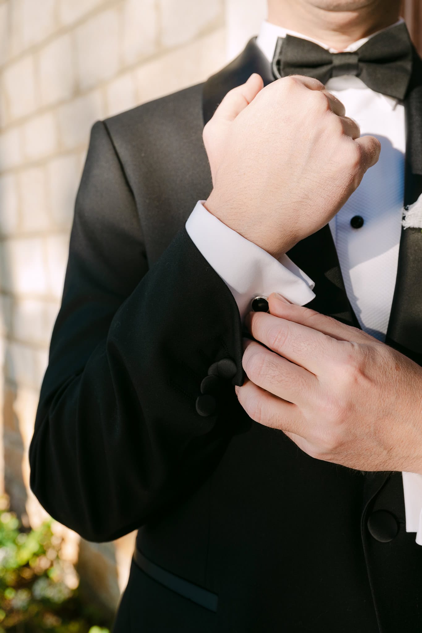 Krupni plan ruku mladoženje koji popravlja manžete na crnom smokingu s leptir mašnom tijekom priprema za vjenčanje.