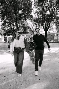 Crno-bijeli kadar nasmijanih roditelja koji tijekom šetnje parkom drže dječaka za ruke i podižu ga u zrak.