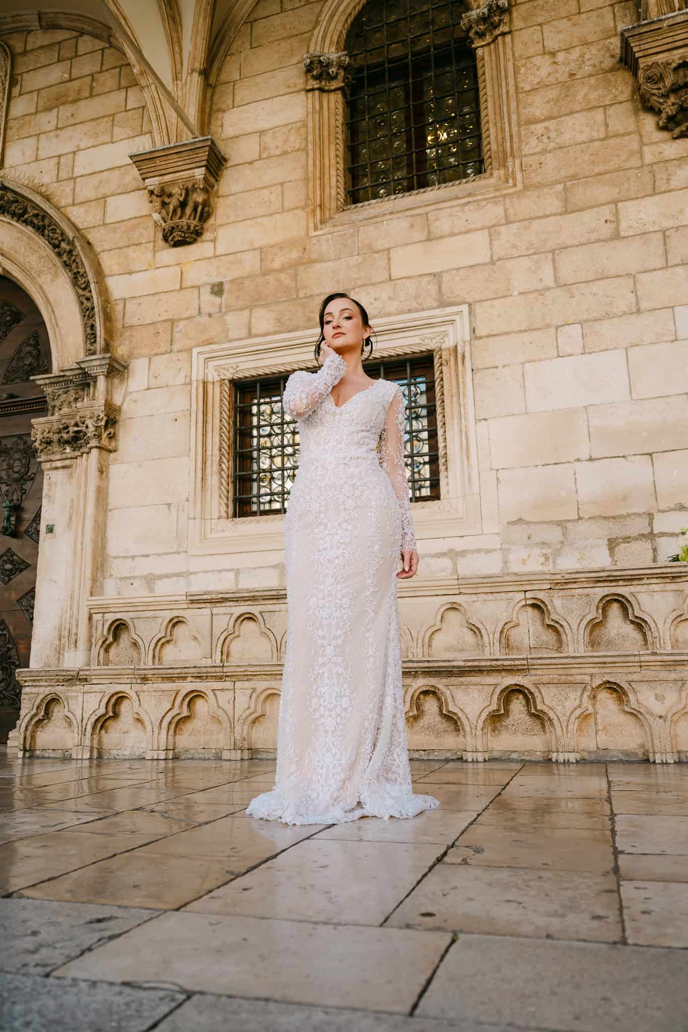 Dubrovnik, Stari grad – portret mladenke na otvorenom; nevjesta u dugoj čipkastoj vjenčanici pozira ispred raskošne povijesne arhitekture s lukovima tijekom outdoor sessiona.