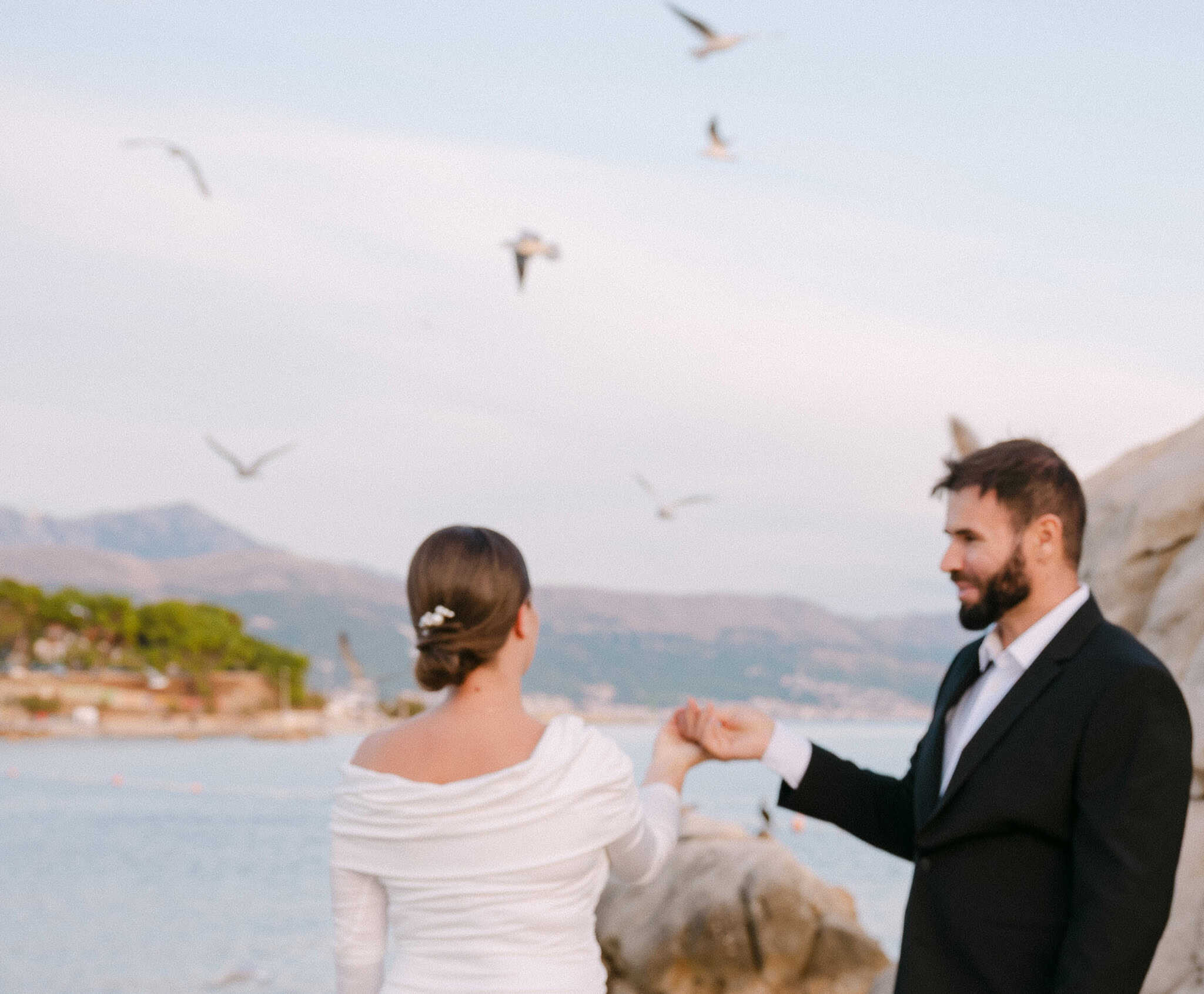 Par u vjenčanom izdanju pleše i drži se za ruke uz more i galebove u pozadini.