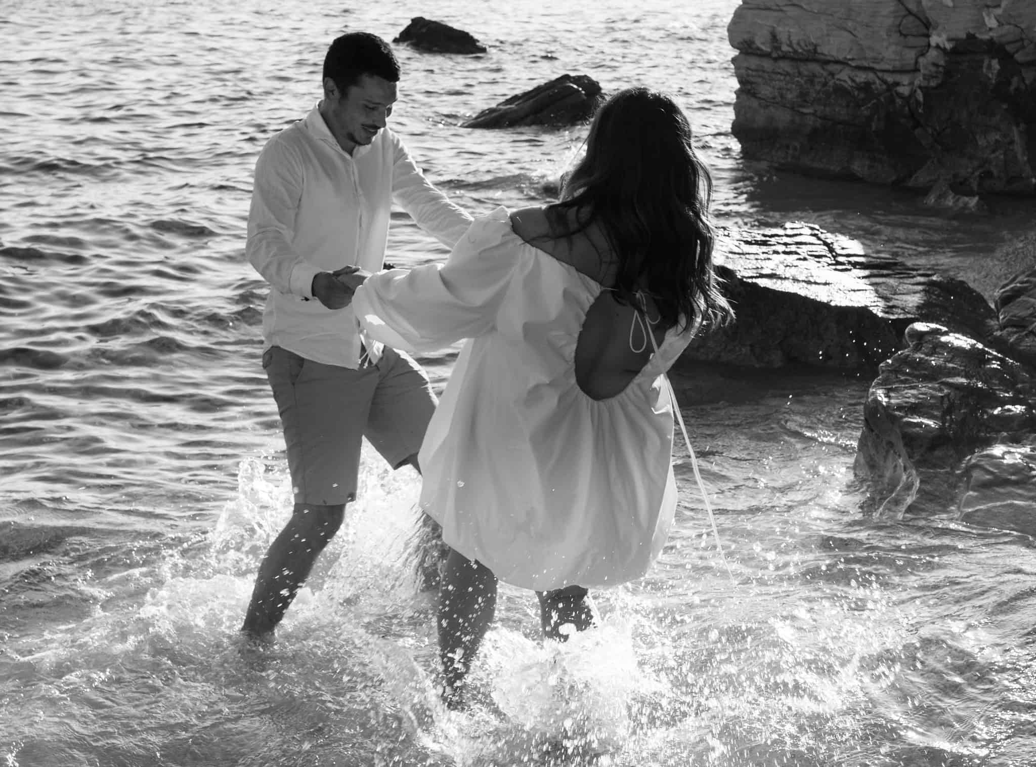 Zaručeni par se igra u moru na plaži, uživajući u zajedničkom trenutku.