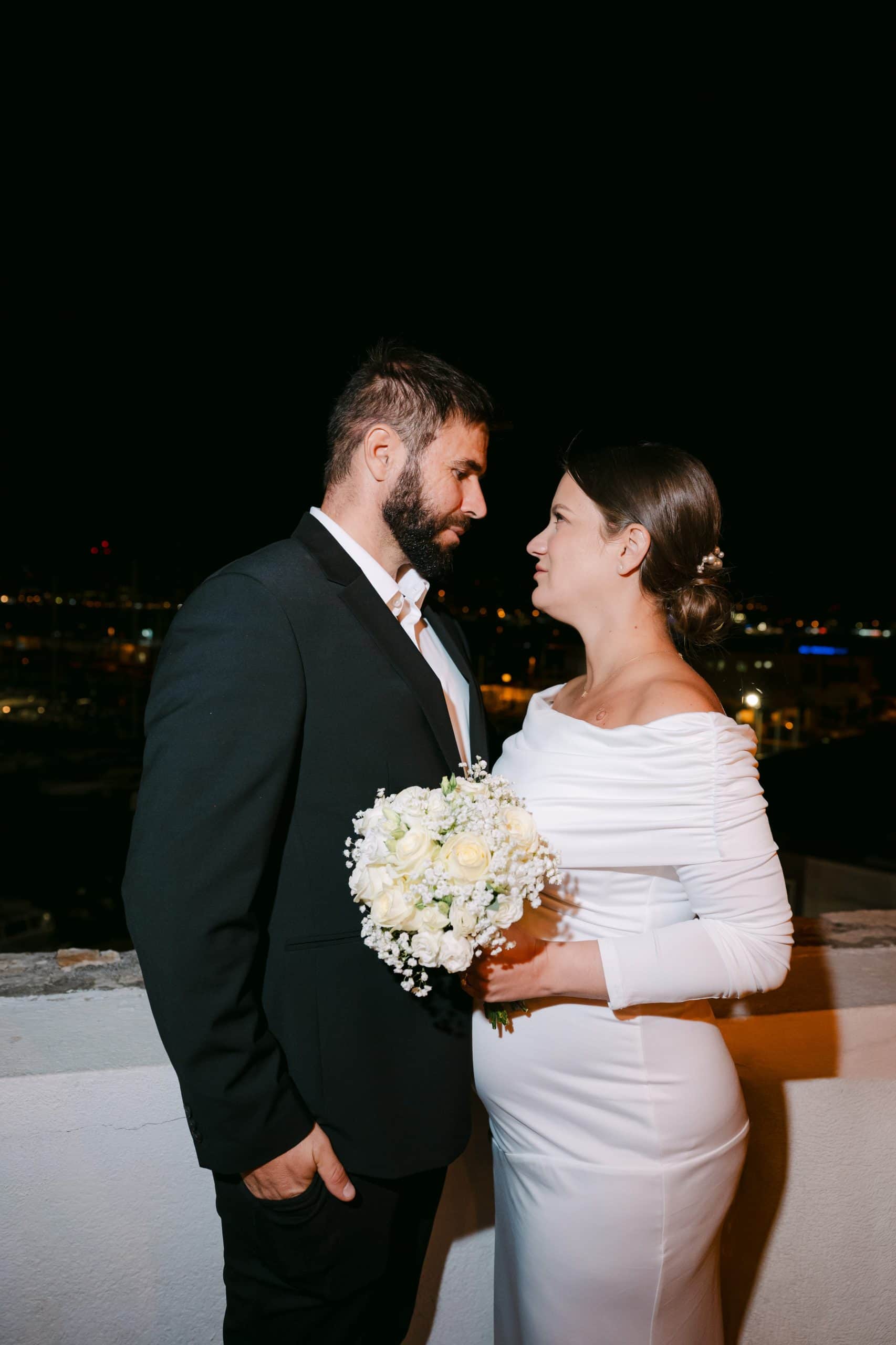 Vjenčana fotografija na terasi s pogledom na grad, mladoženja i nevjesta gledaju jedan drugog.