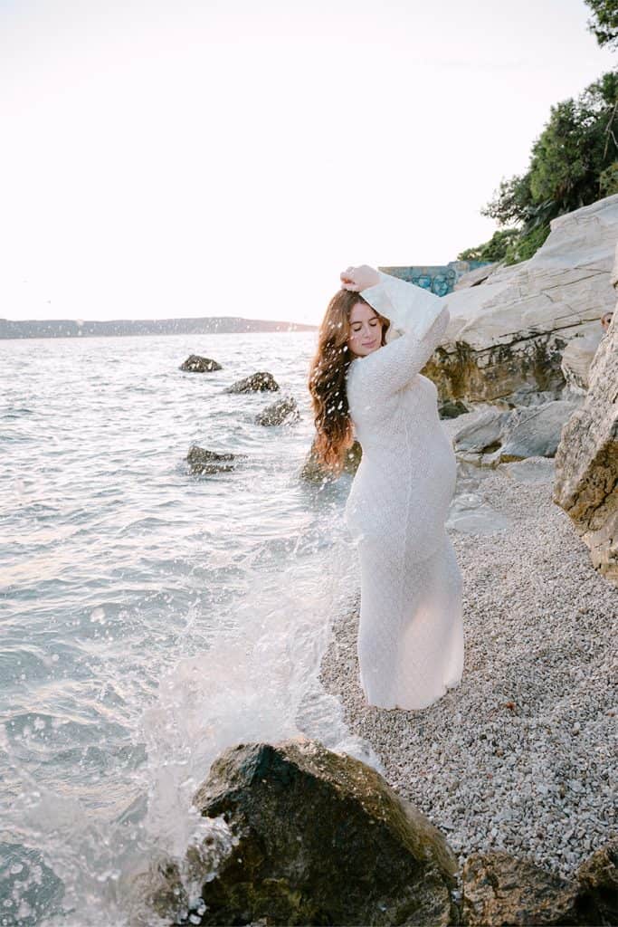 Buduća majka na plaži s prirodnim okruženjem i morem u pozadini.