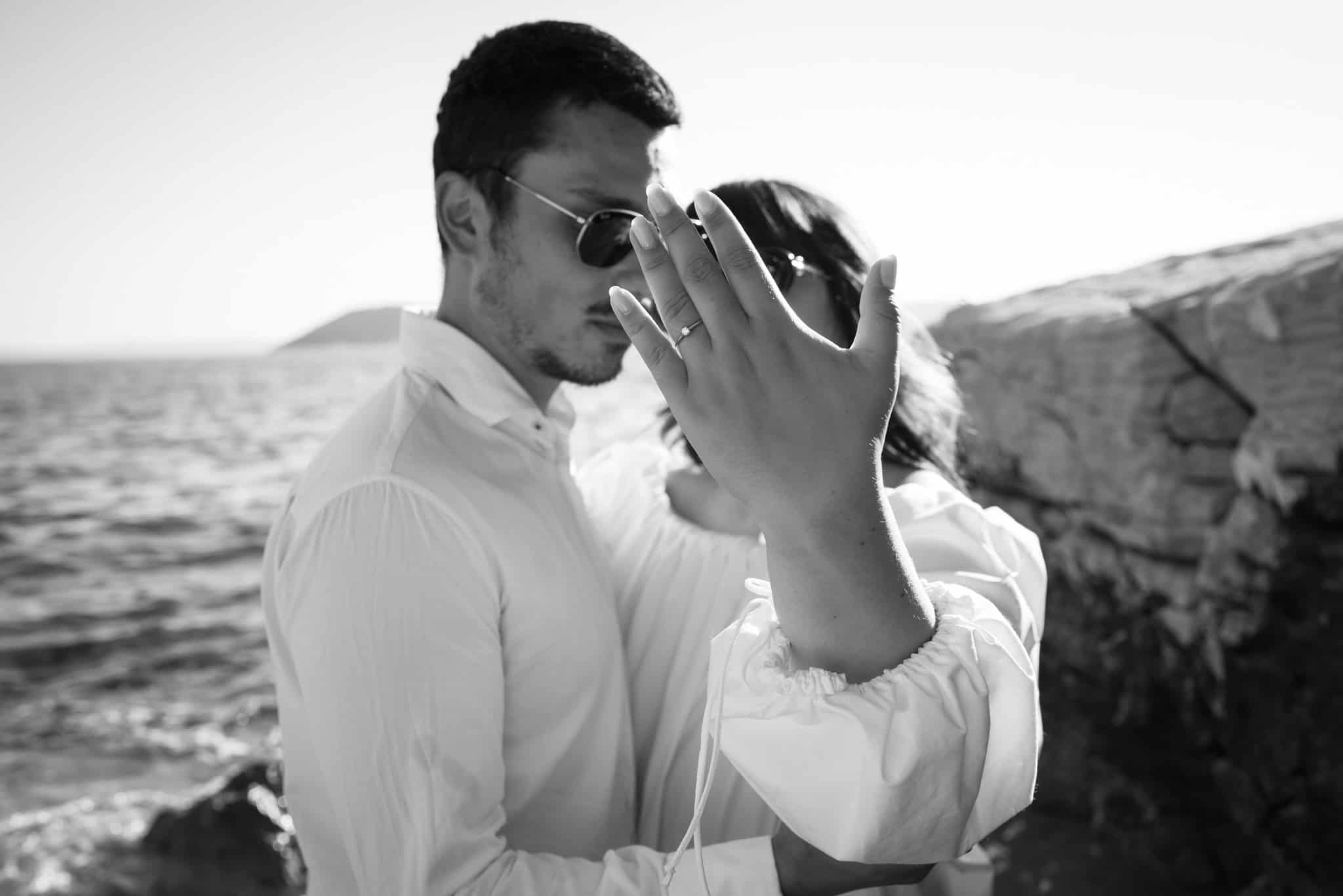 Crno-bijeli kadar zaručnika; krupni plan ruke s prstenom u prvom planu.