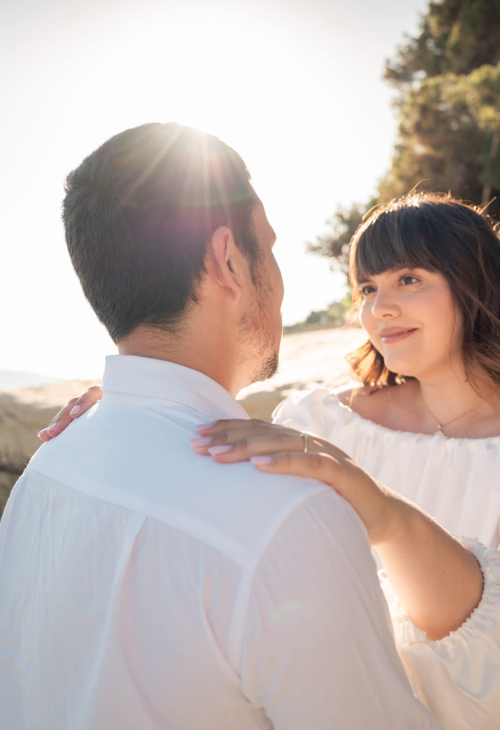 Ljubavni par na plaži uz zalazak sunca i zelenilom u pozadini.
