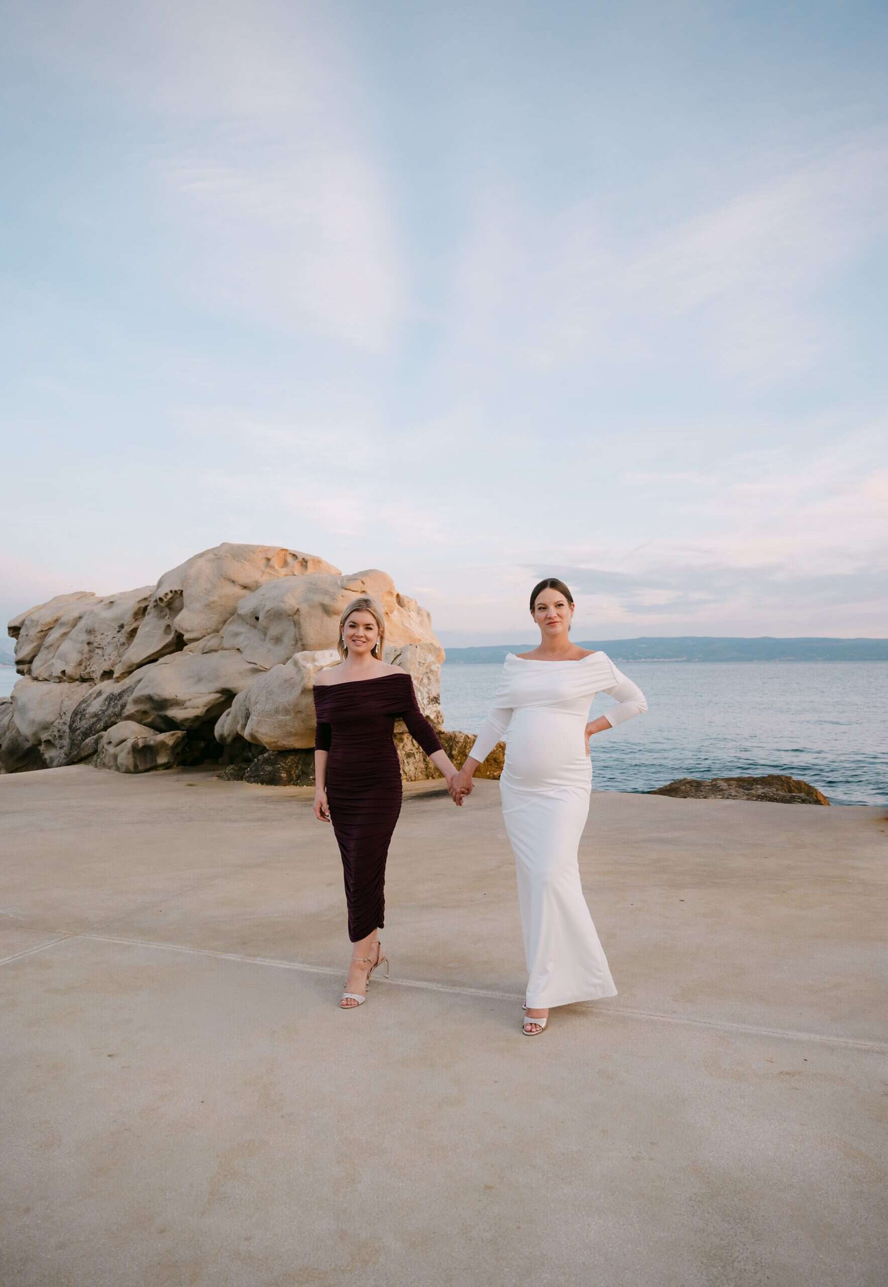 Mladenka i kuma u elegantnim haljinama, drže se za ruke uz more na plaži Bačvice.