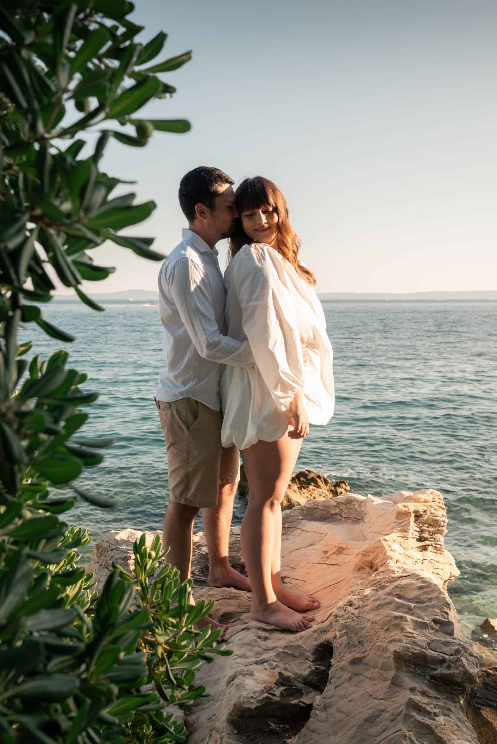 Budući mladenci Petra i Ivan na obali mora, romantična scena na stijeni uz zalazak sunca, prirodna i intimna atmosfera.