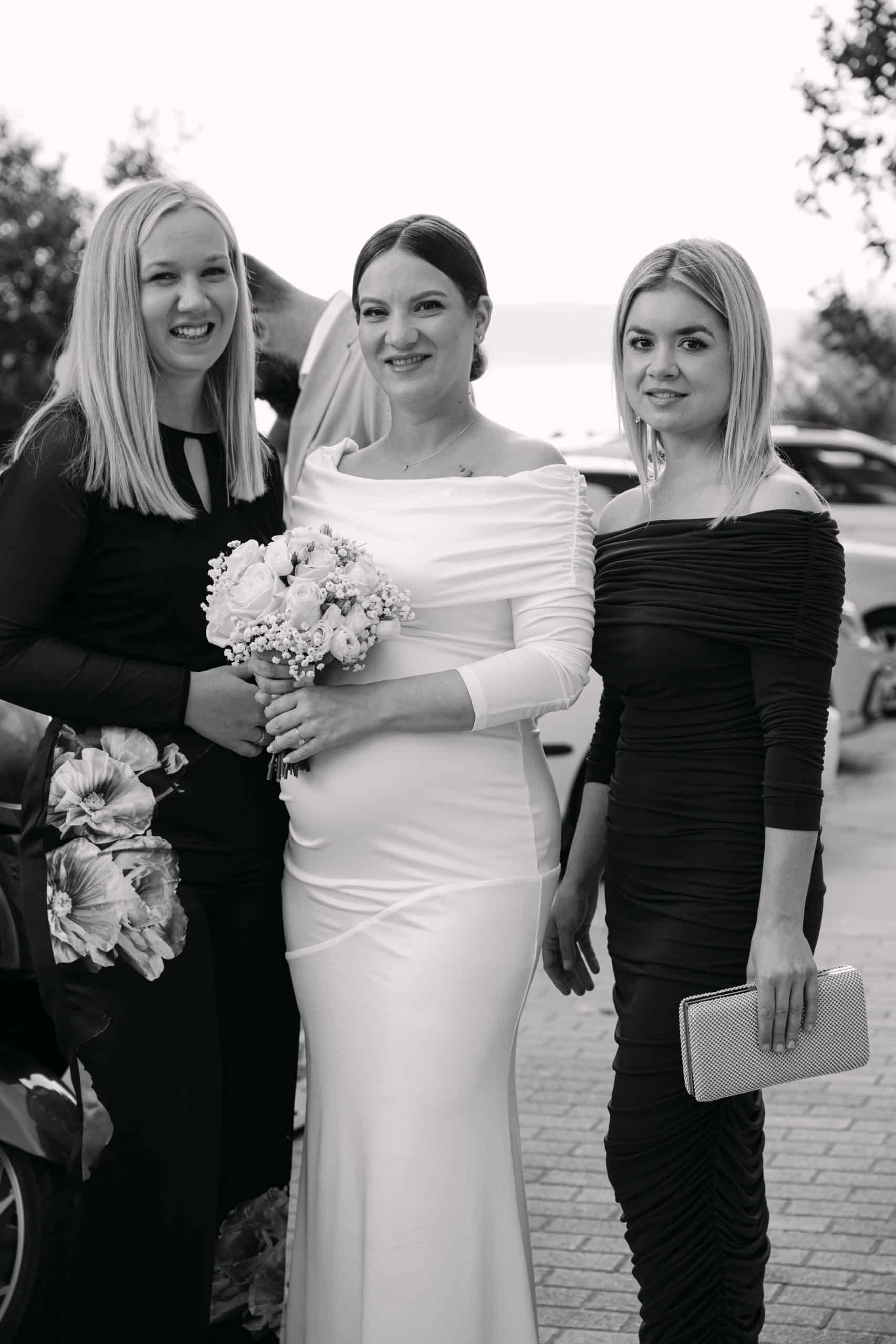 Vjenčana fotografija s prijateljicama na otvorenom, svečane haljine i osmijehi, prirodna pozadina.