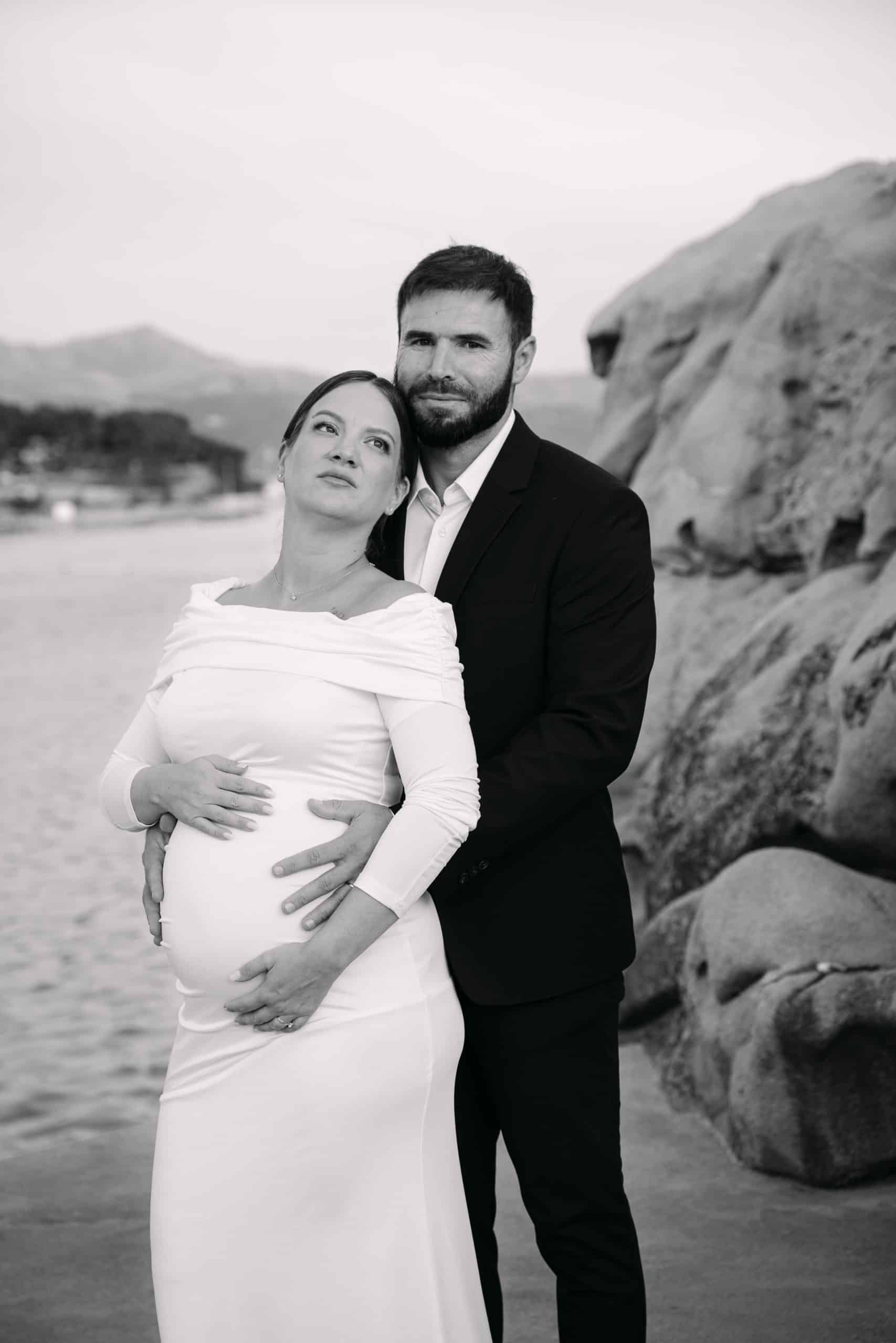 Trudna mladenka i mladoženja na crno-bijeloj fotografiji s plaže.