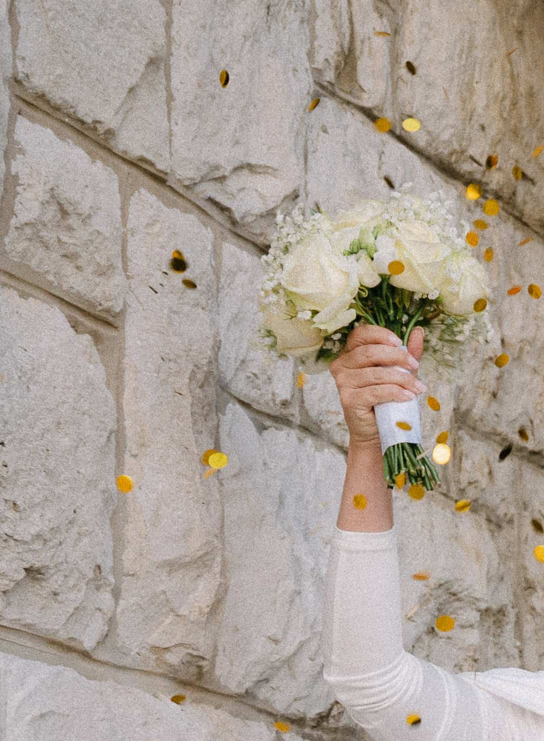 Mladenka drži vjenčani buket od bijelih cvjetova s ručno vezanim vrpcom.