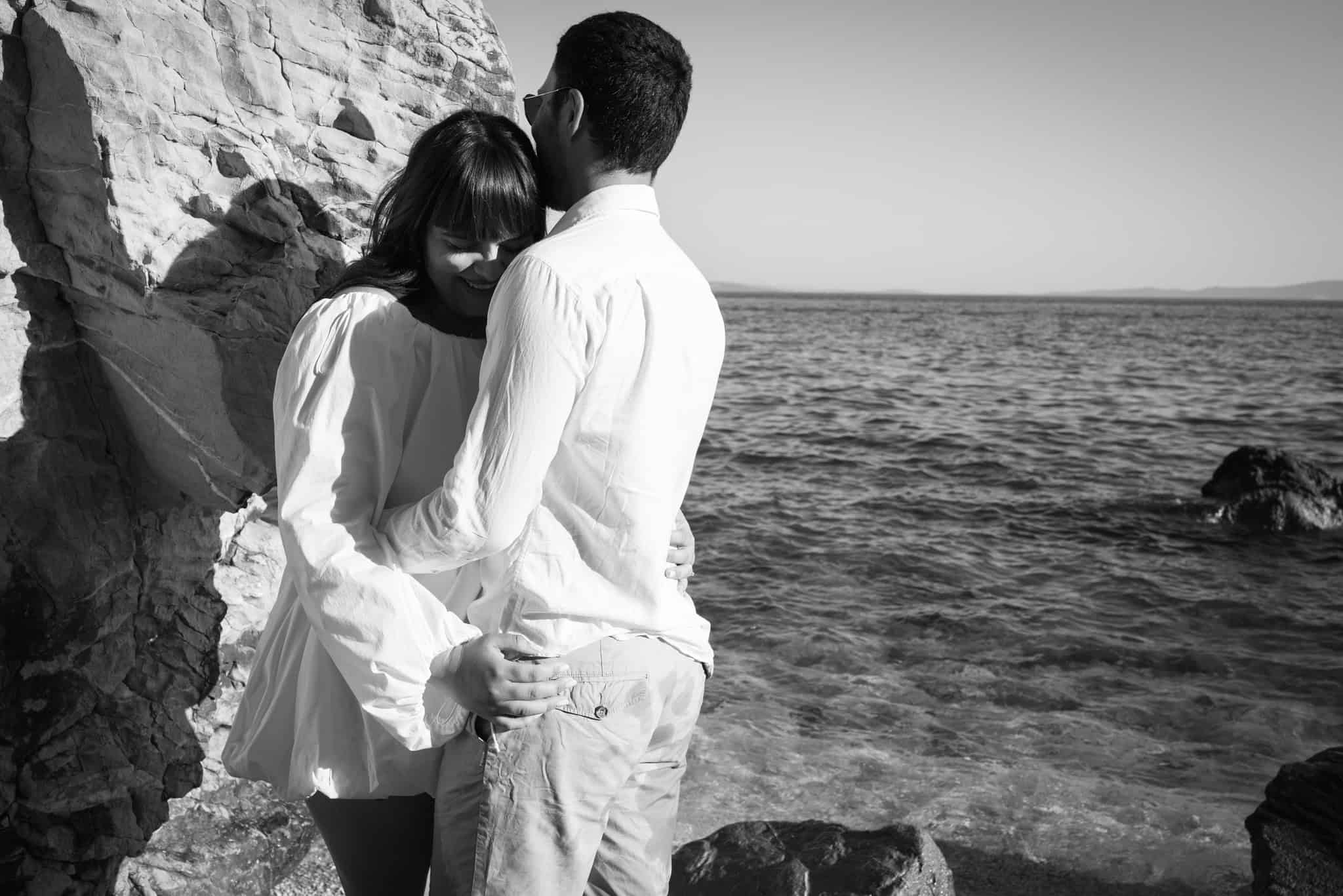 Ljubavni par na obali mora, snimljeno u crno-bijeloj tehnici, prikazuje spontano romantični trenutak uz more.