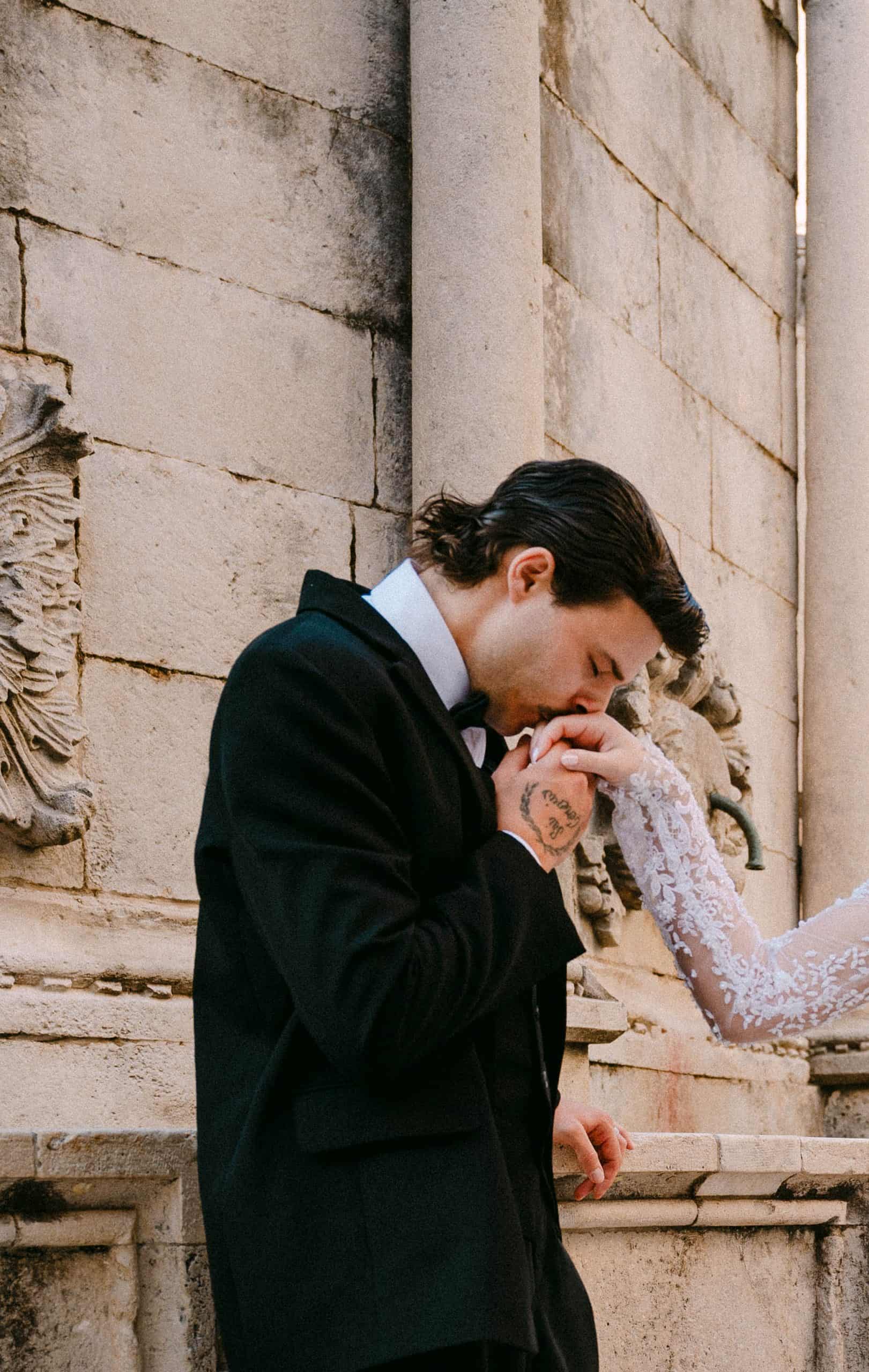 Dubrovnik wedding session - krupni plan poljupca u ruku; mladoženja ljubi ruku nevjesti s naglaskom na detalje čipkaste vjenčanice i tetovažu.