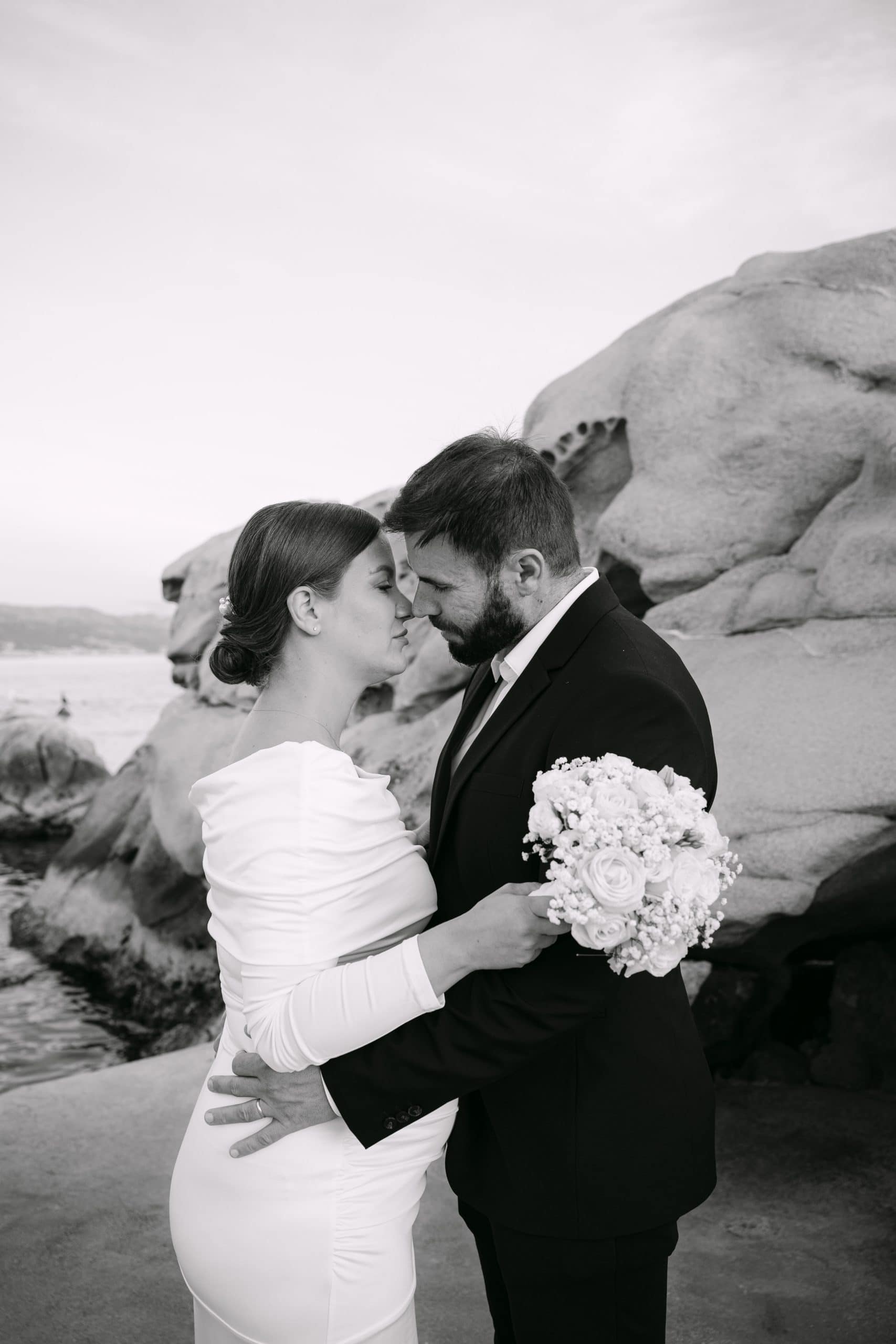 Mladenka i mladenoženja stoje priljubljeni jedno uz drugo na betonskom platou uz more.