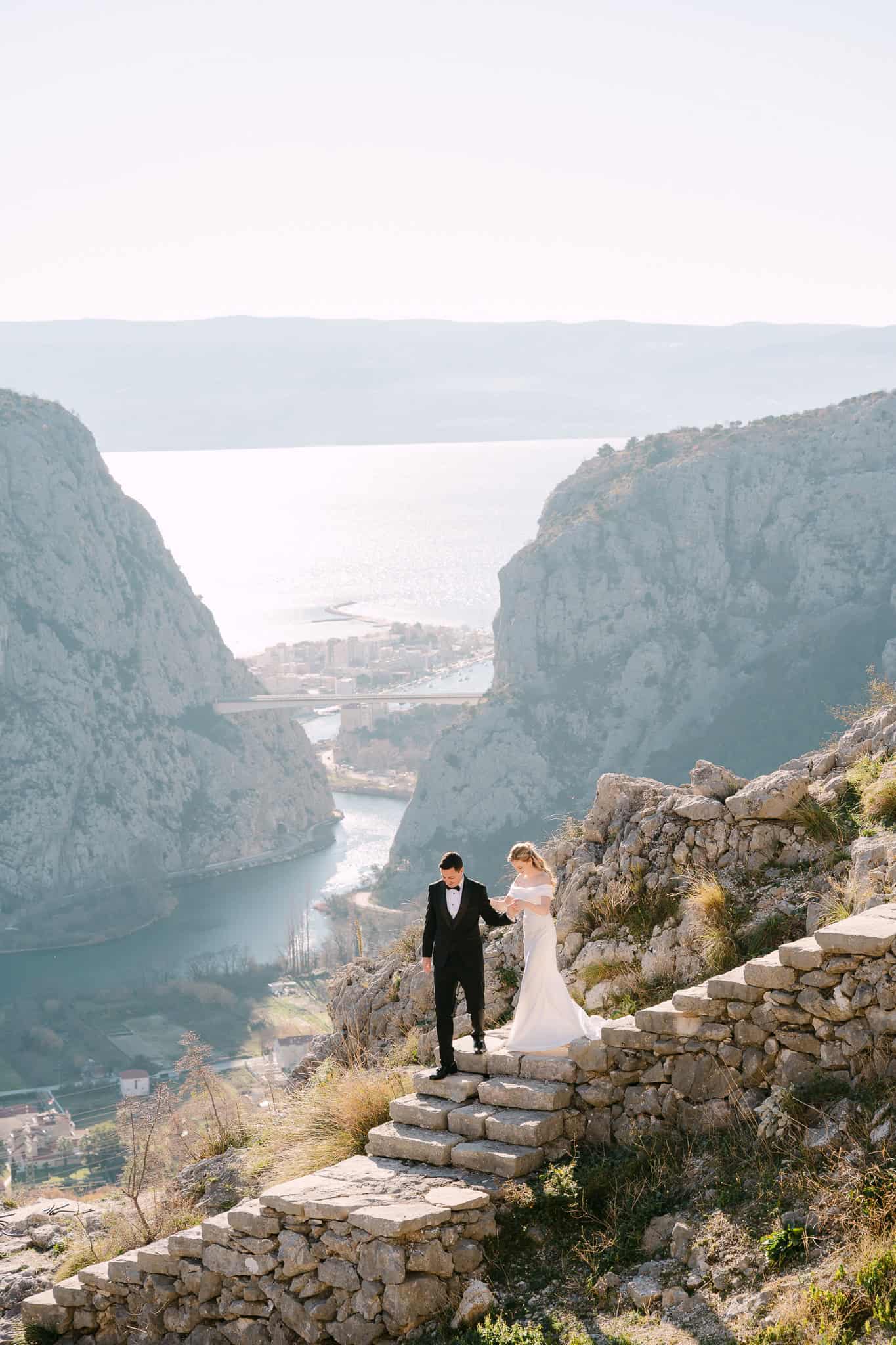 Mladenci se drže za ruke i silaze niz kamene stepenice s pogledom na litice i rijeku Cetinu.