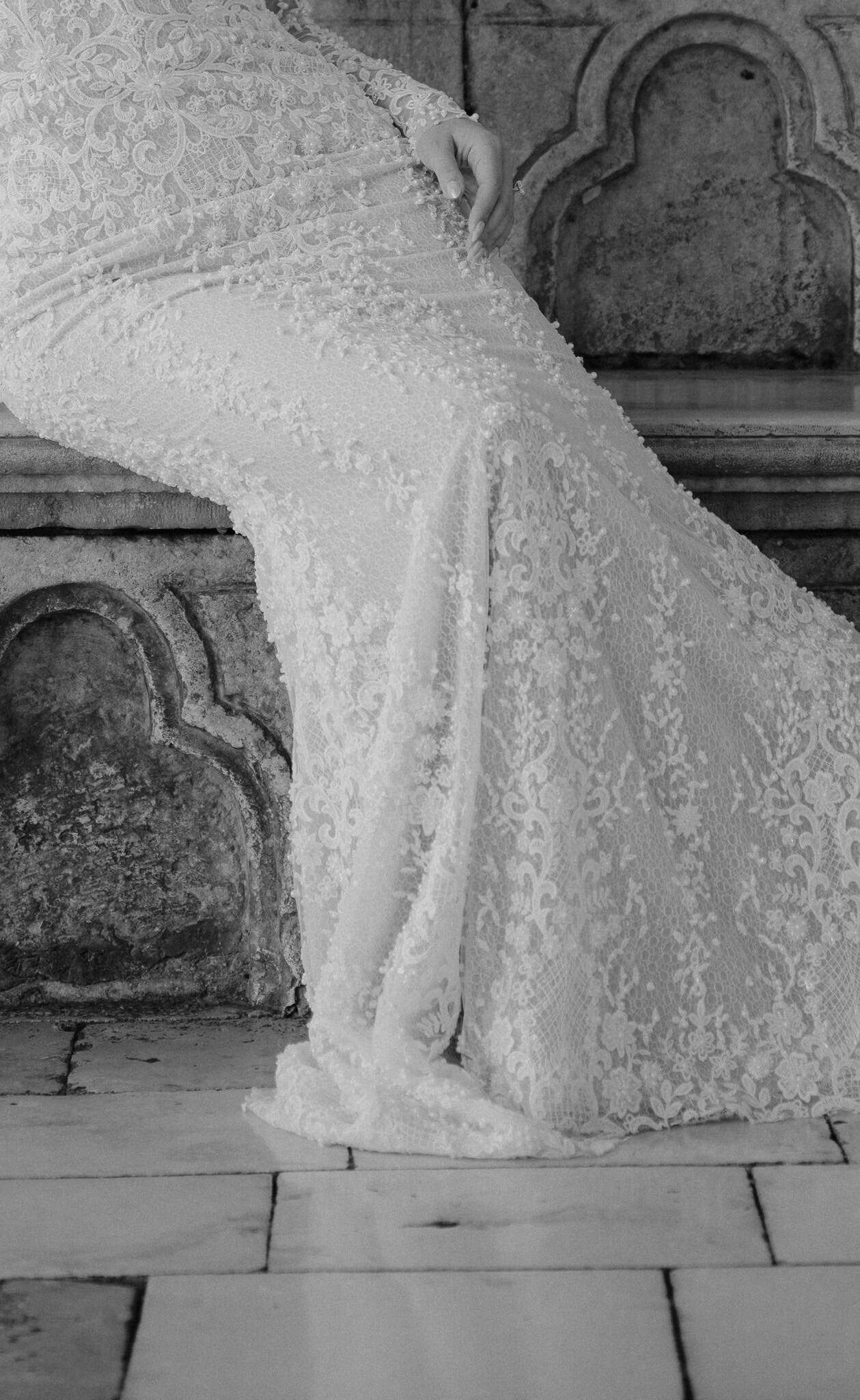 Dubrovnik vjenčanje - crno-bijeli detalj vjenčanice; bogata čipka mladenkinog dugačkog šlepa prostire se preko povijesne kamene klupe.