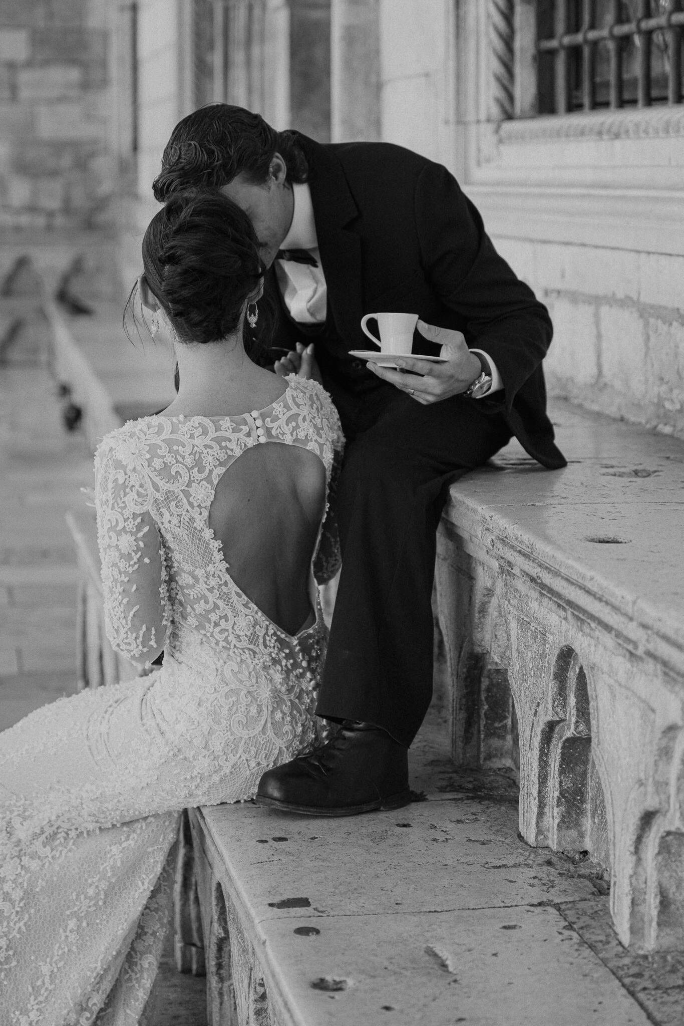 Dubrovnik wedding session - mladoženja i mladenka sjede na kamenoj klupi, s naglaskom na otvorena leđa elegantne čipkaste vjenčanice.