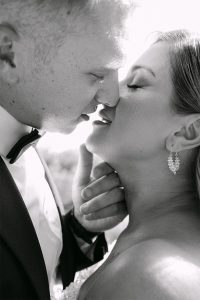 Crno-bijeli krupni plan lica mladenaca u intimnom trenutku poljupca na svadbenom fotografiranju.