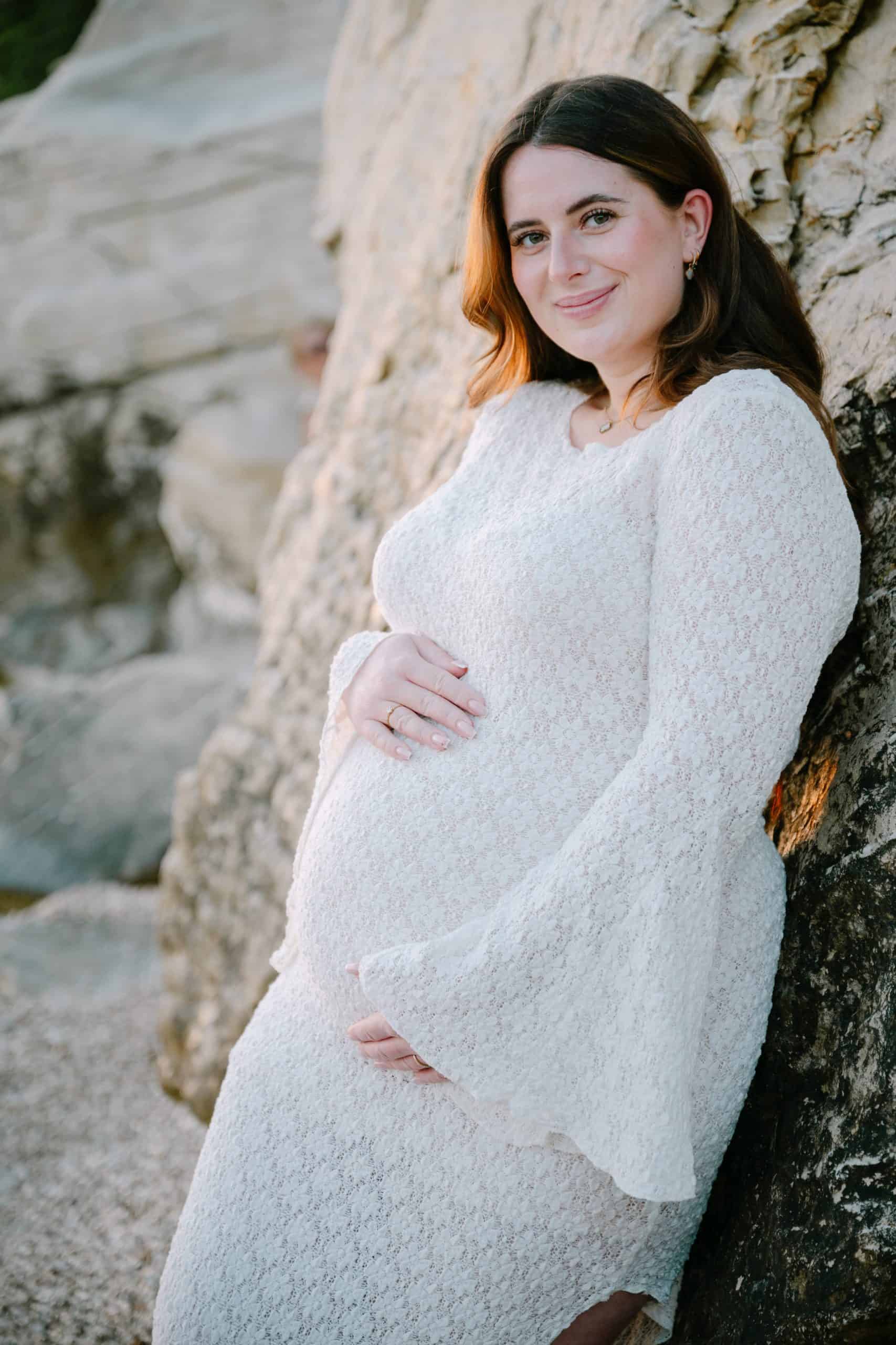 Trudnica se smiješi na otvorenom blizu stjenovitog krajolika, fotografiranje trudnoće.