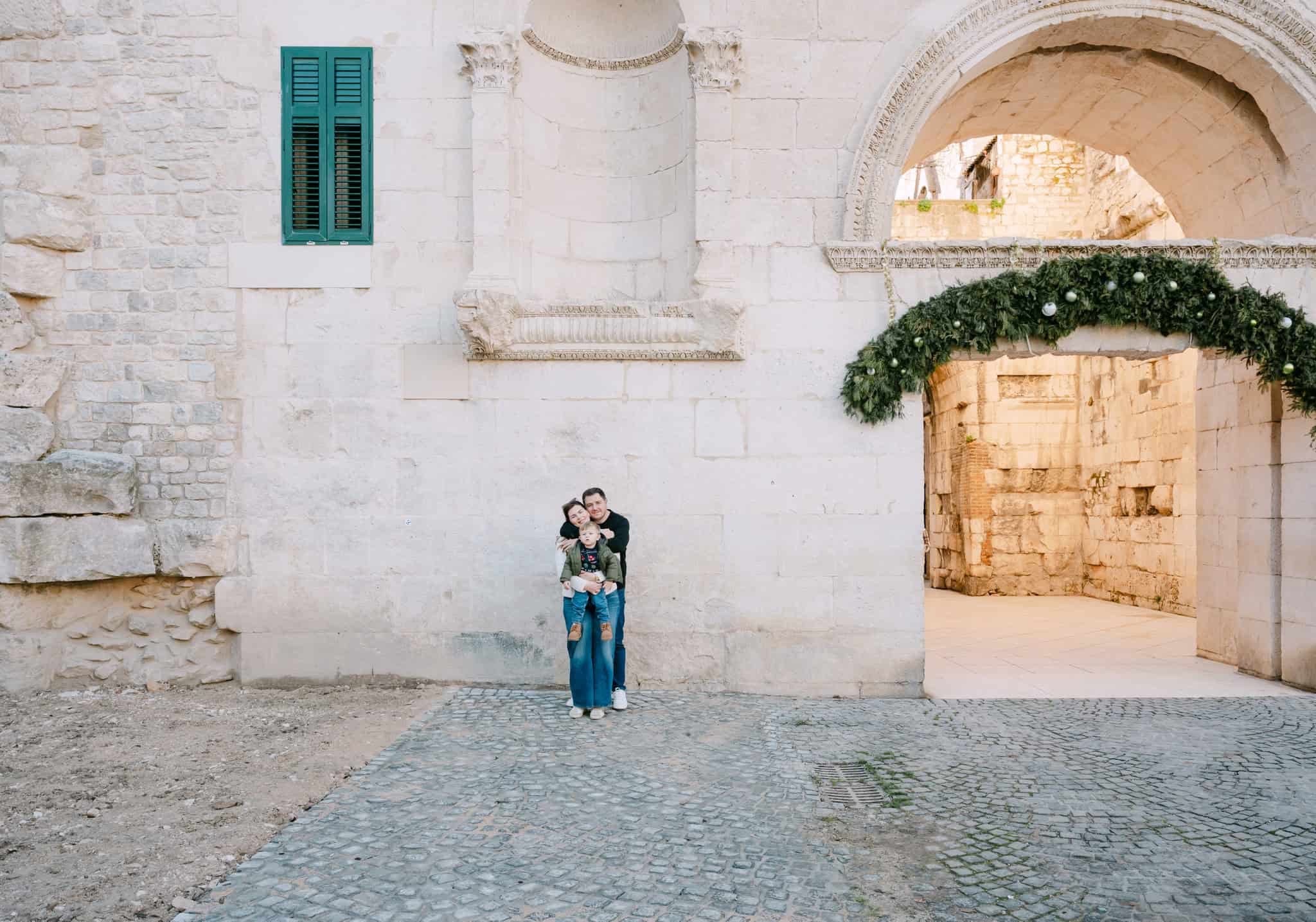 Obitelj se grli ispred povijesnog kamenog zida s lukom u gradu Splitu.