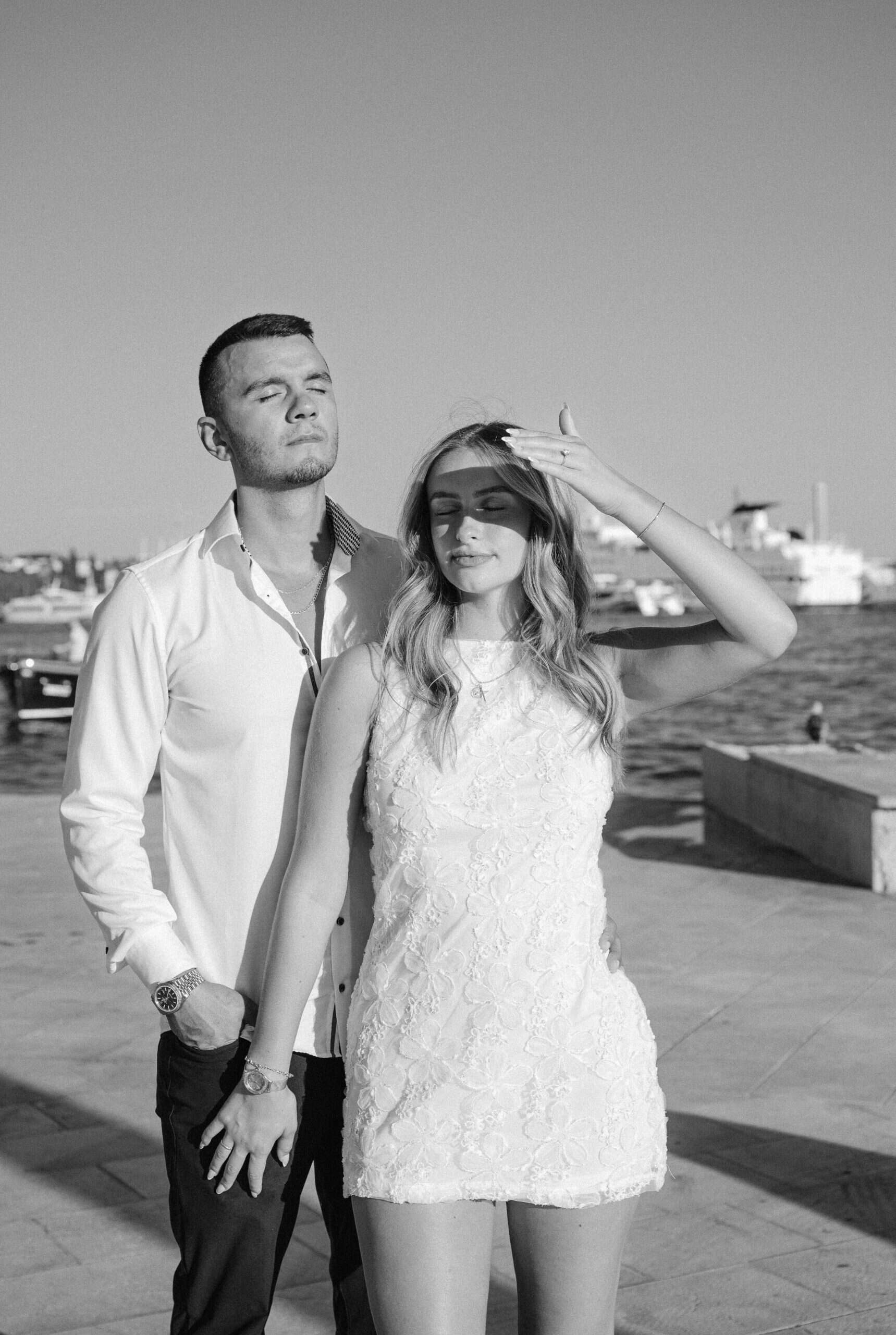 Ljubavni par na obali, romantična fotografija u crno-bijeloj boji, vizura splitske luke u daljini.