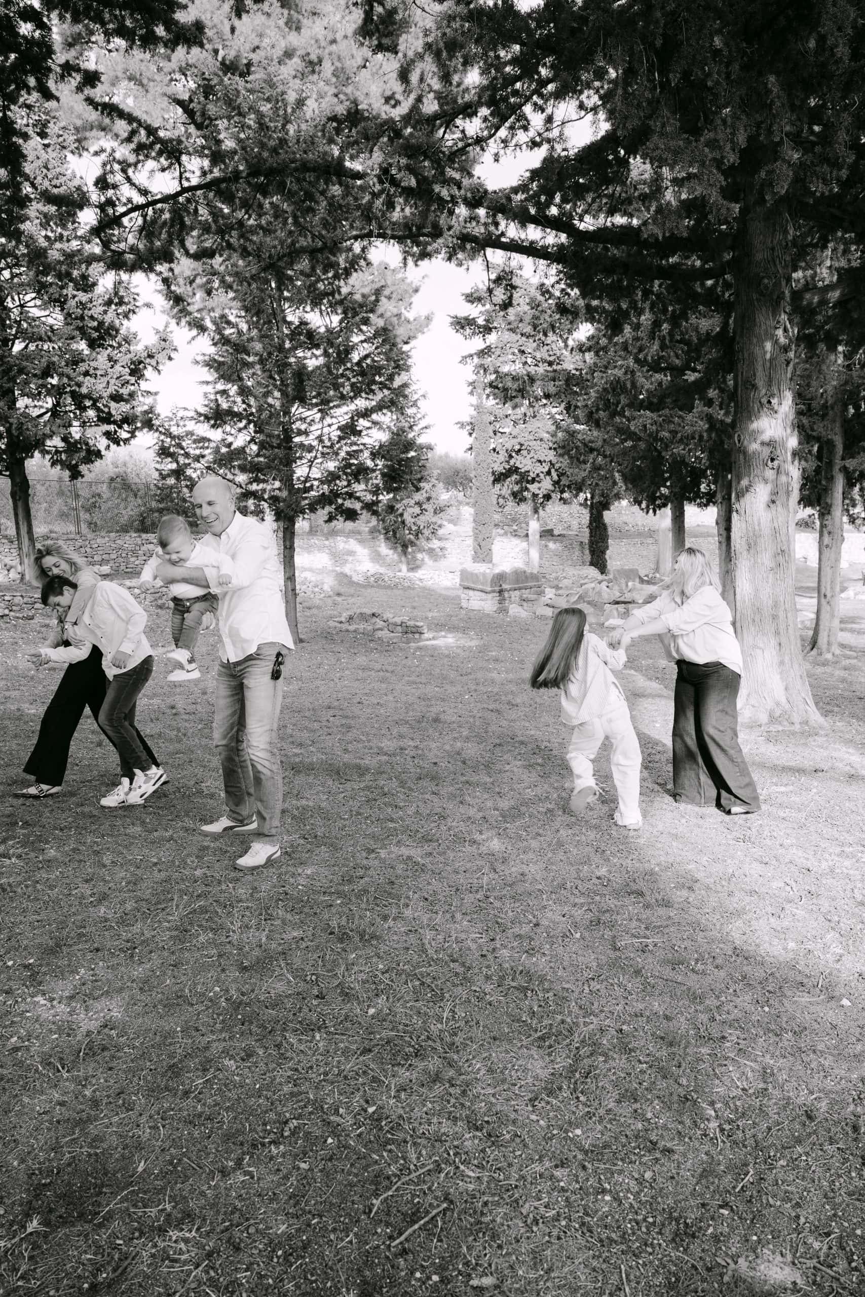 Obitelj uživa u vremenu provedenom na otvorenom u parku s visokim drvećem i otvorenim prostorom.