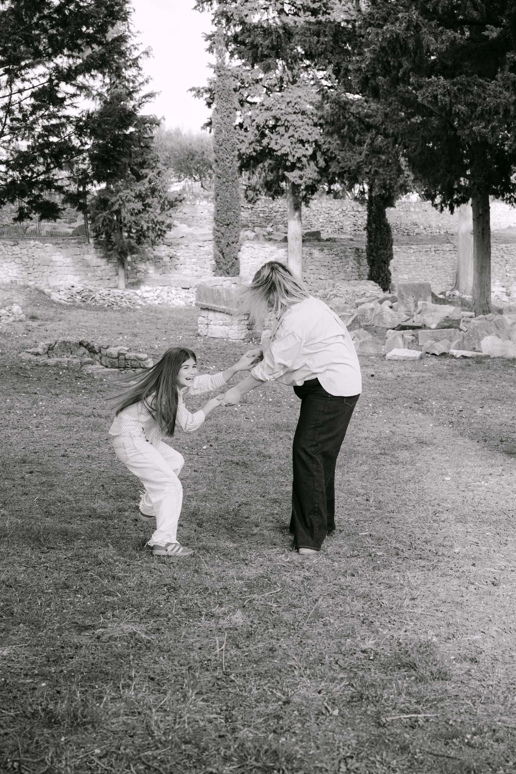 Majka i kćerka drže se za ruke, uživajući u razigranom trenutku u prirodi.