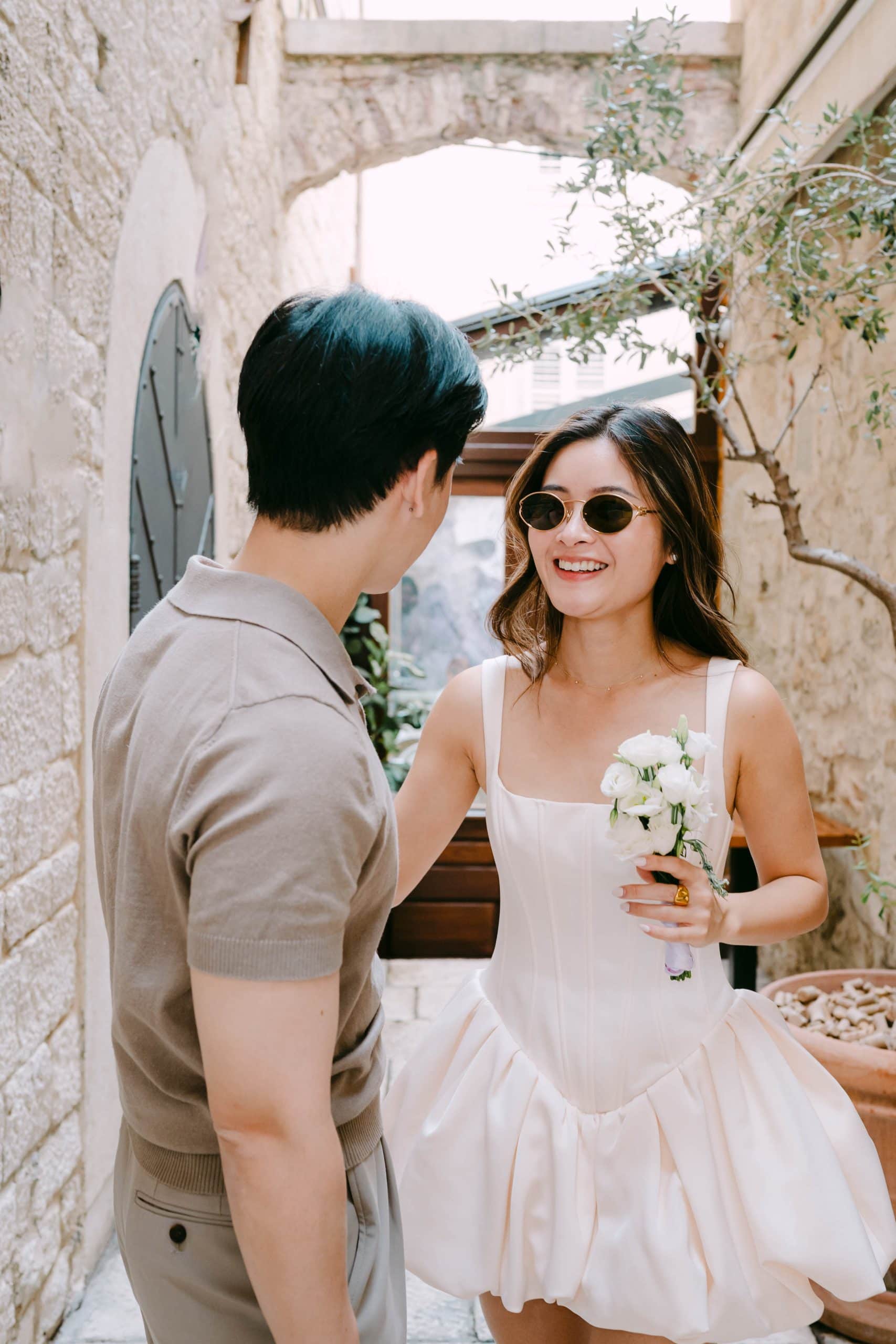 Elegantna žena koja drži buket, kraj muža u ležernoj odjeći.