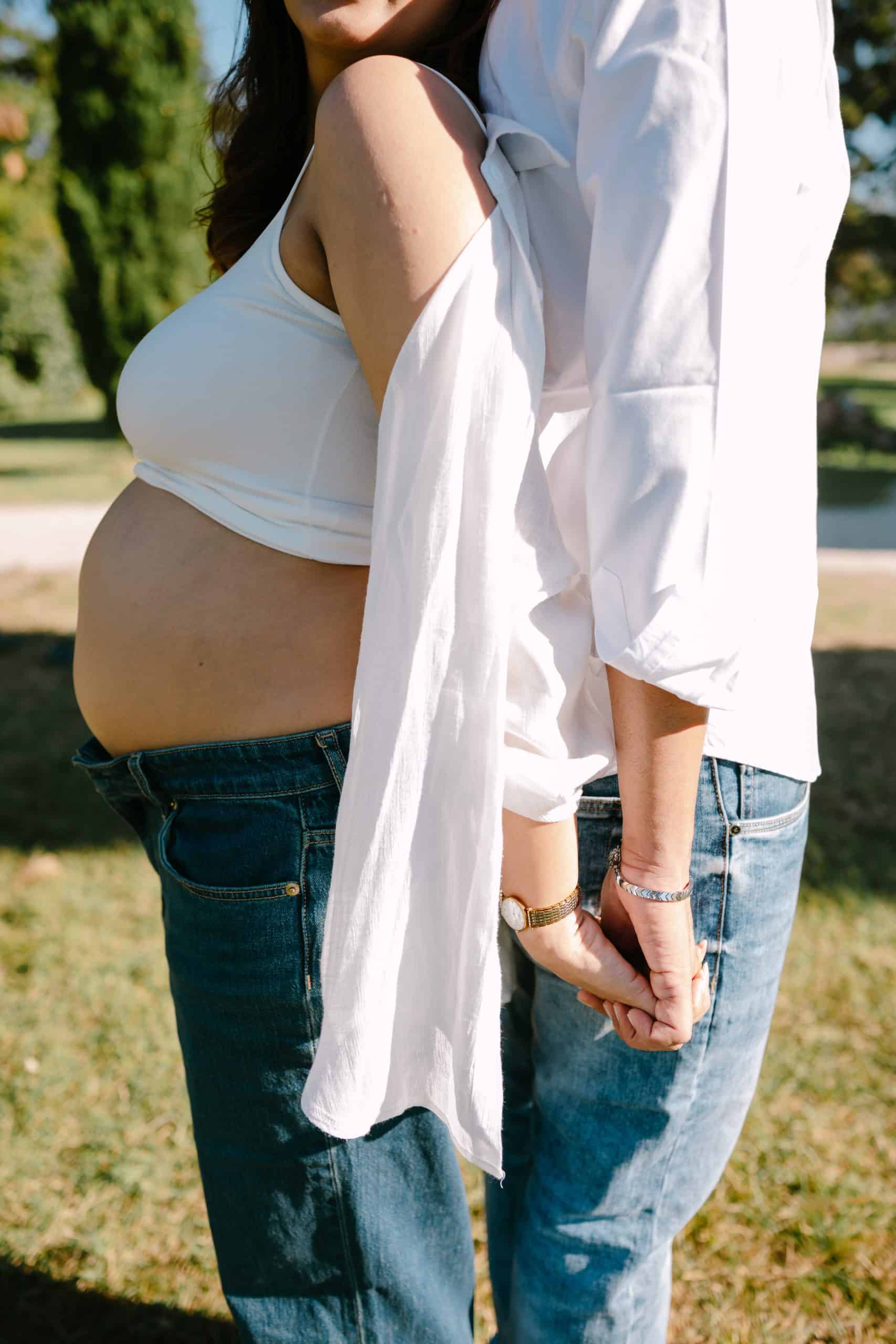 Trudna majka i suprug drže se za ruke naslonjeni leđima jedan na drugoga.