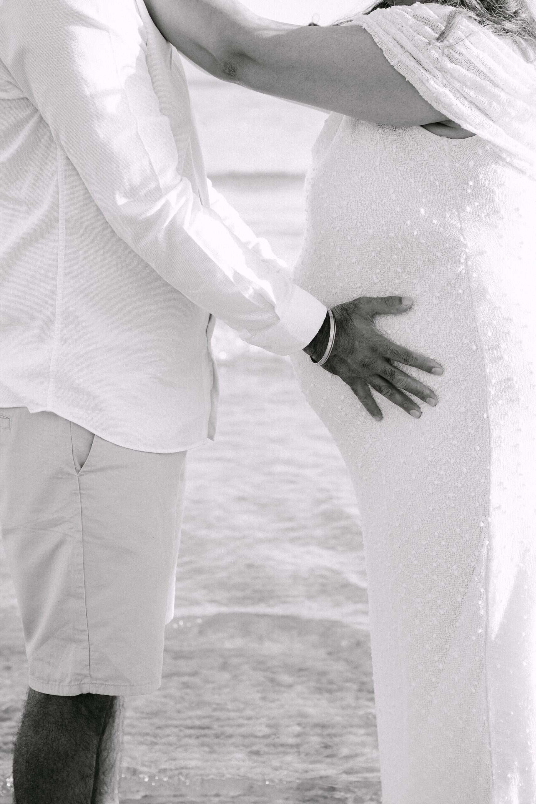 Trudnica i partner drže trbuh na plaži, slaveći trudnoću i ljubav.