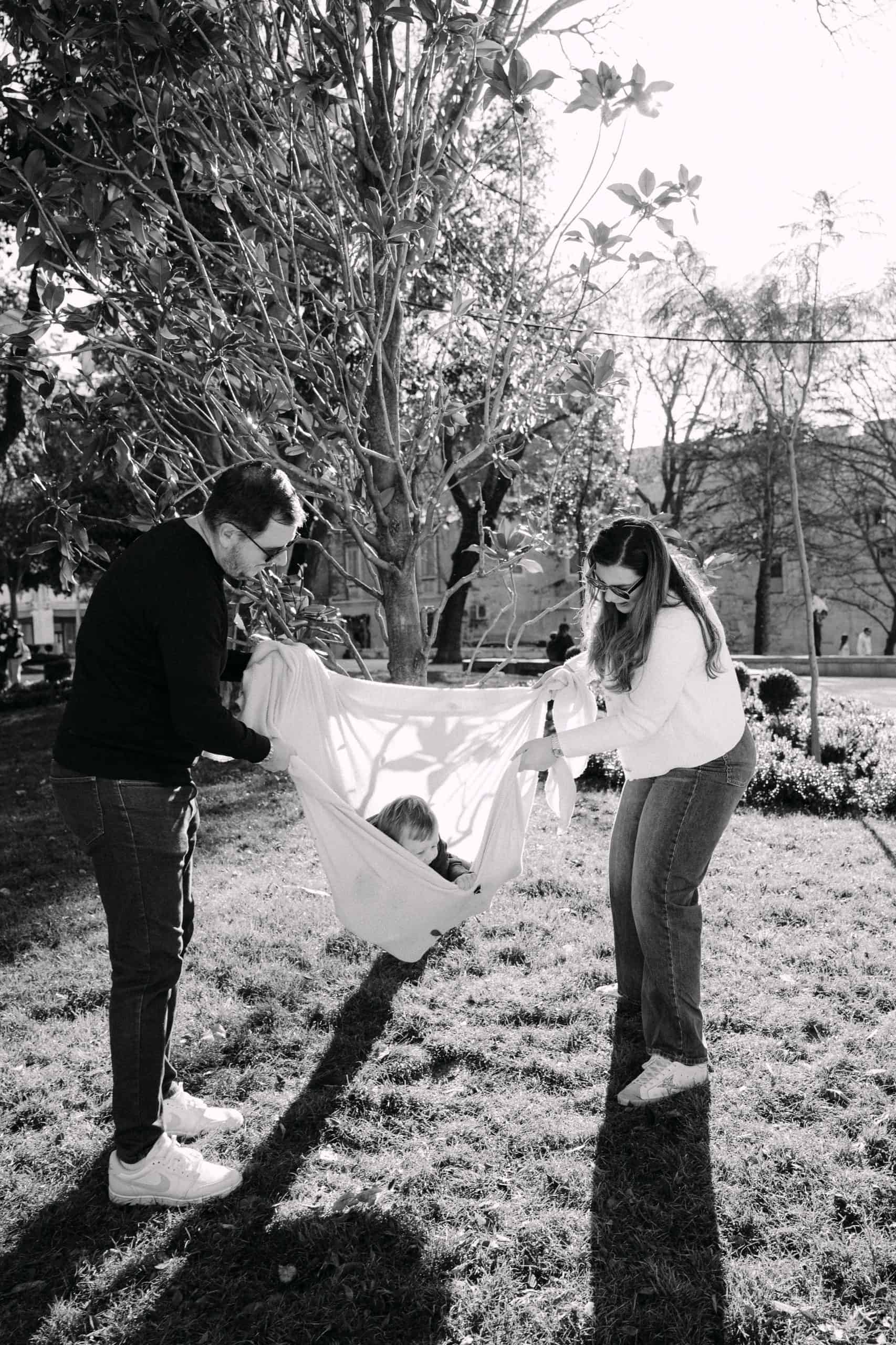 Obitelj se igra u parku s visećom mrežom između drveća.