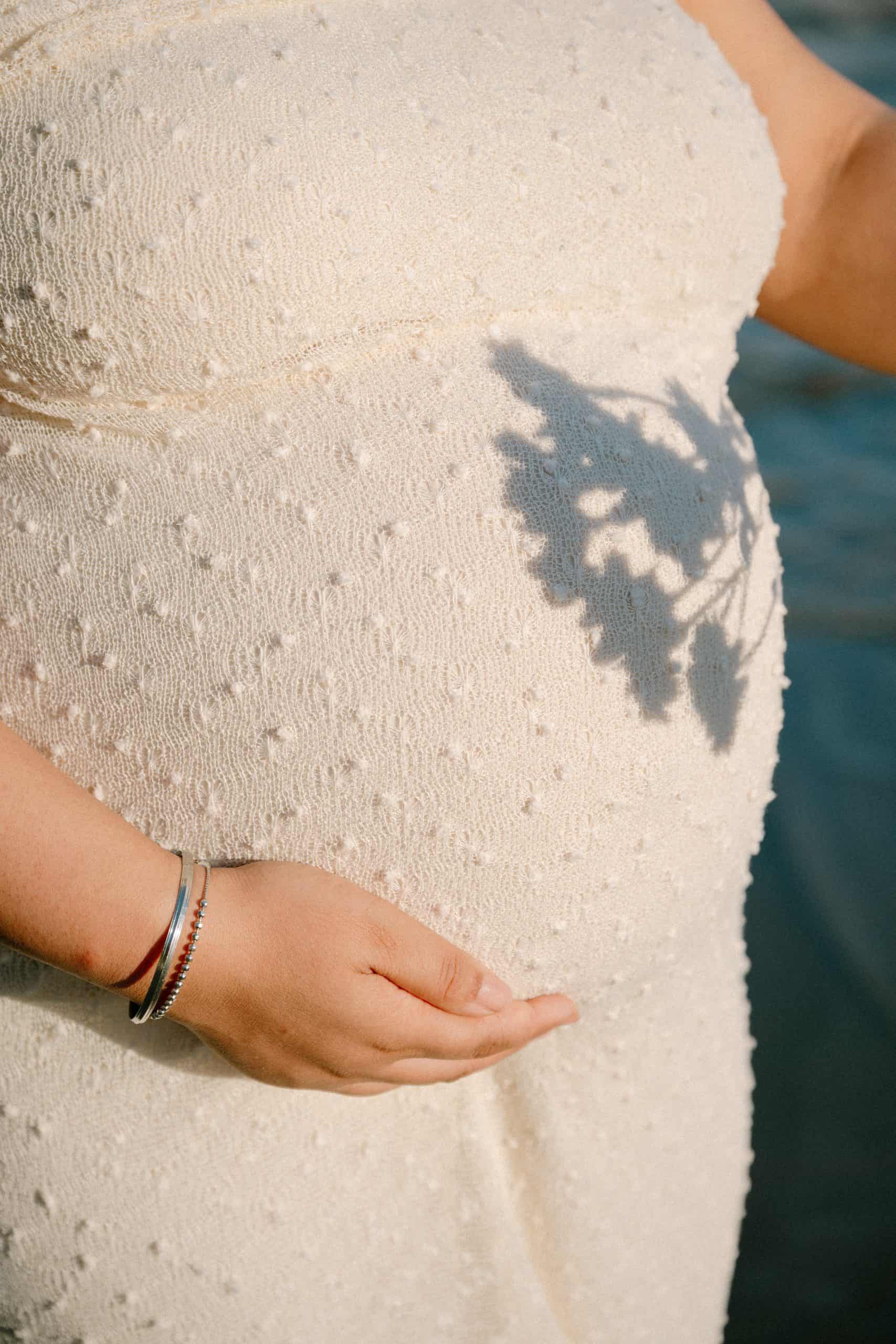 Trudnica drži svoj trbuh sa sjenom cvijeta na haljini.